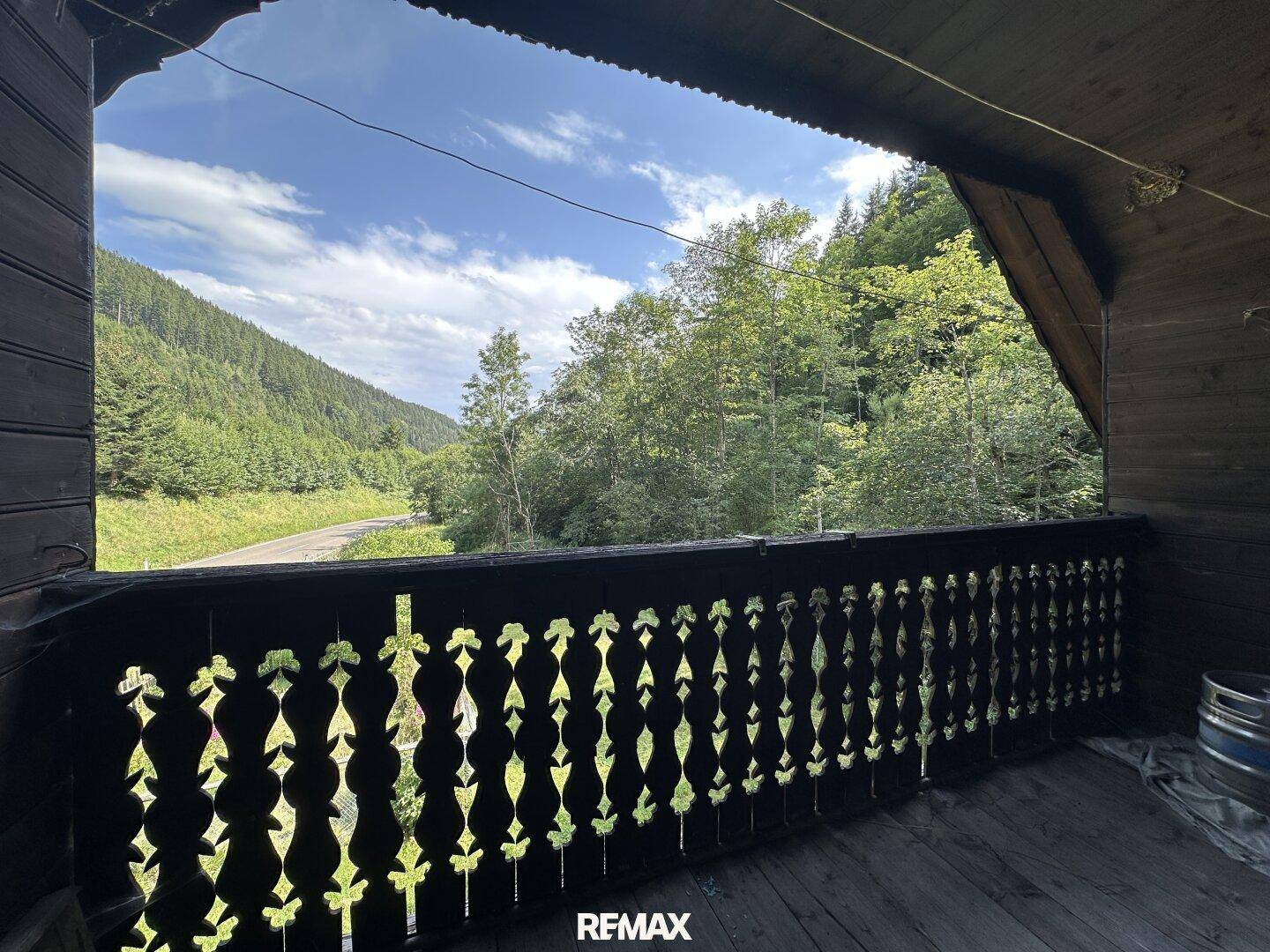 Traditioneller Holzbalkon mit geschnitztem Geländer und weitem Blick auf die grüne Landschaft.