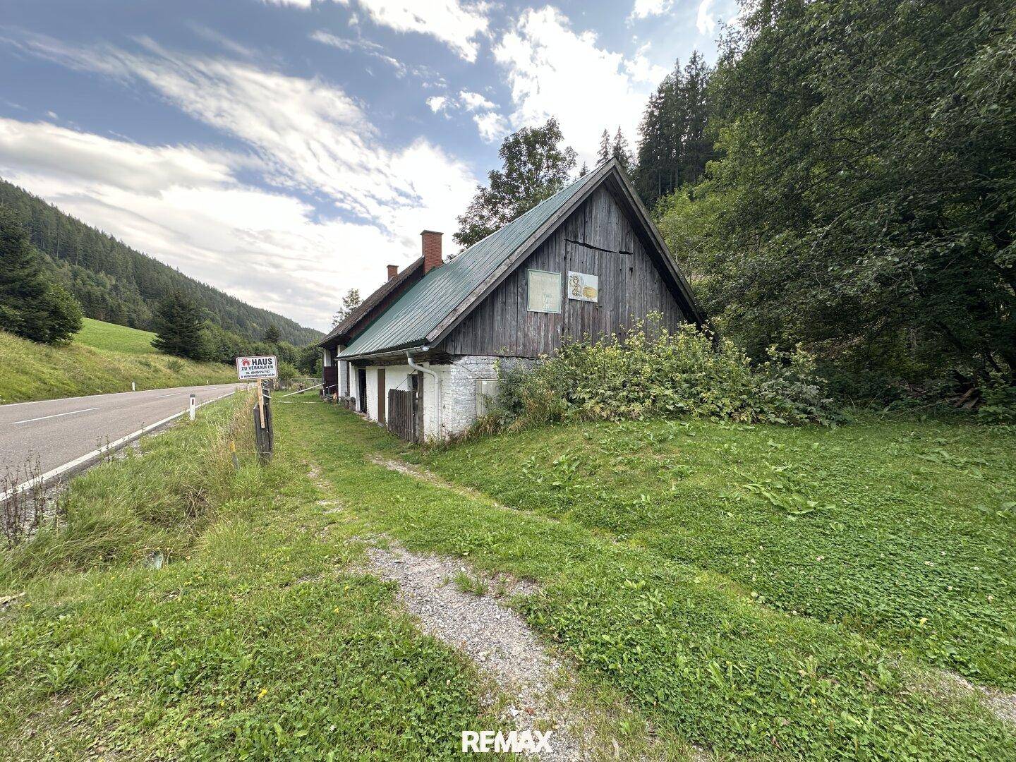 Altes, rustikales Holzhaus mit grünem Dach und umliegender Natur in einer Berglandschaft.