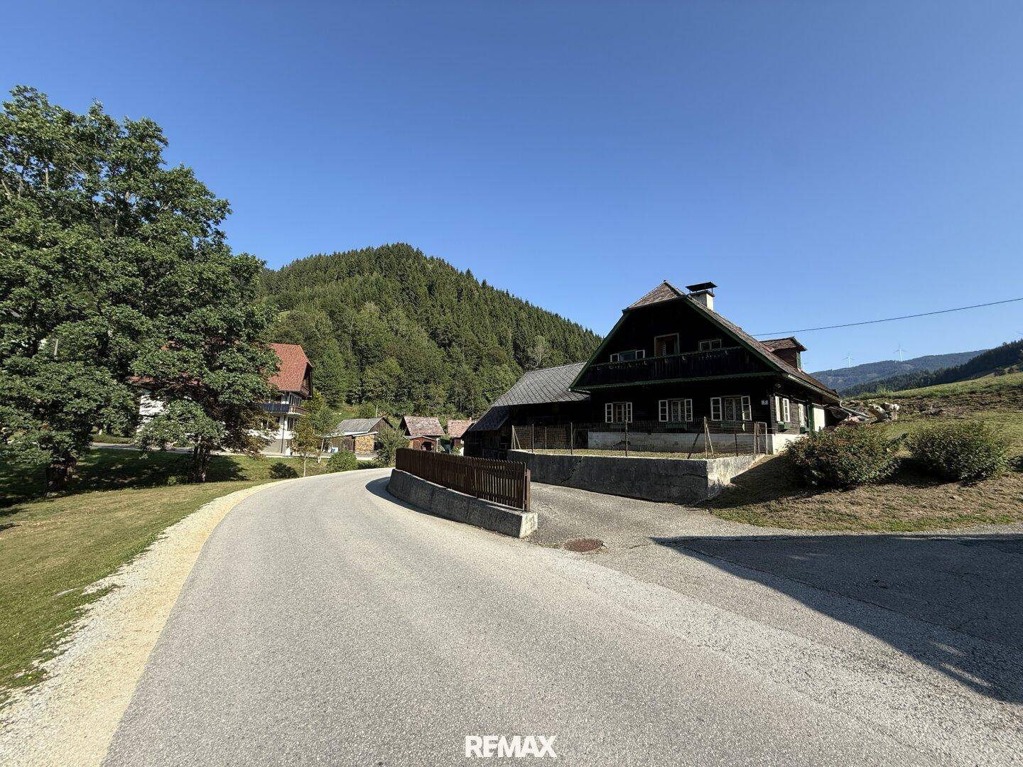Landstraße führt zu einem traditionellen Holzhaus, eingebettet in eine idyllische Berglandschaft.
