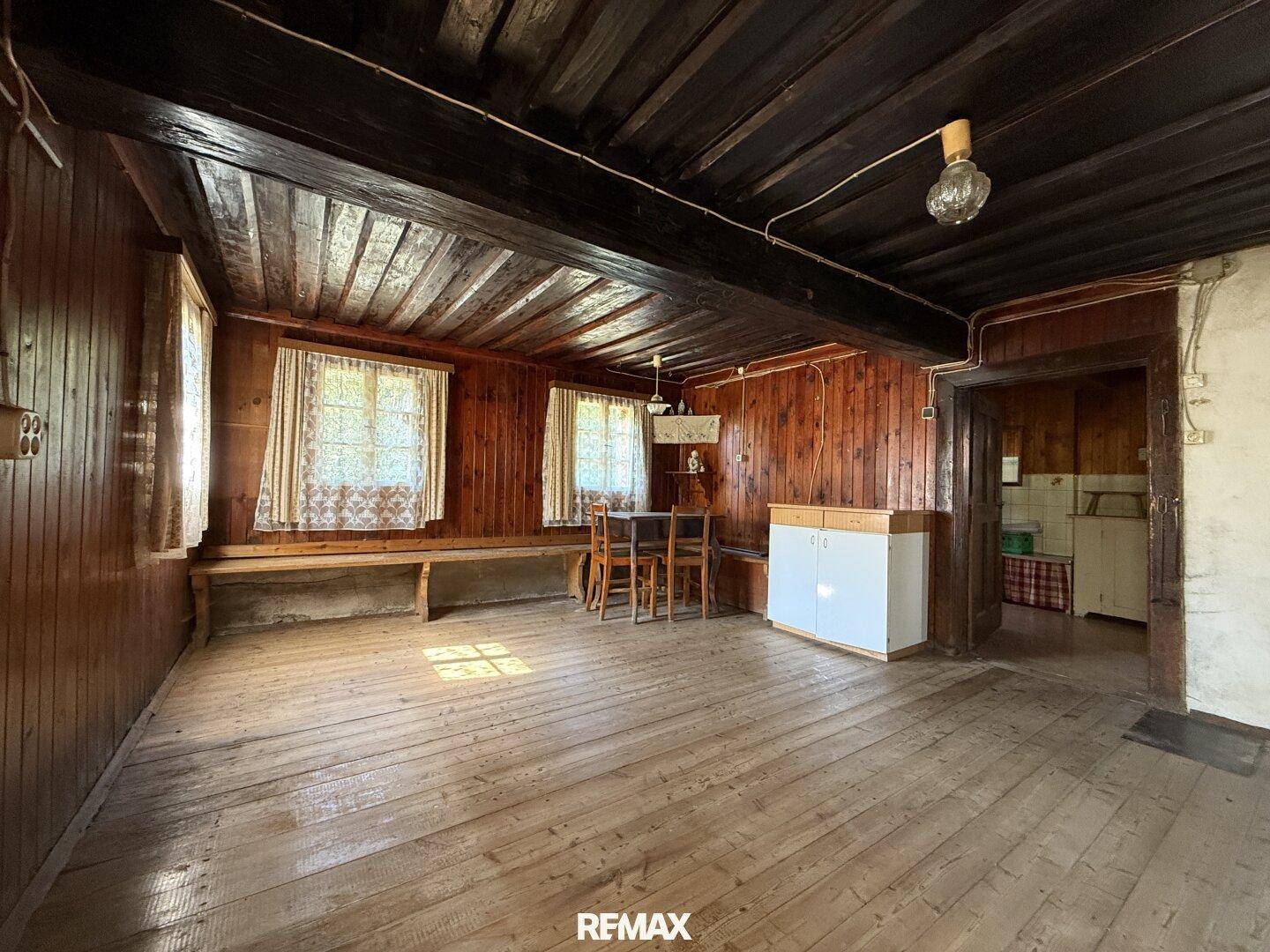Rustikaler Wohn-Essbereich mit Holzböden, Holzvertäfelung und traditionellen Möbeln, hell durch Fenster.