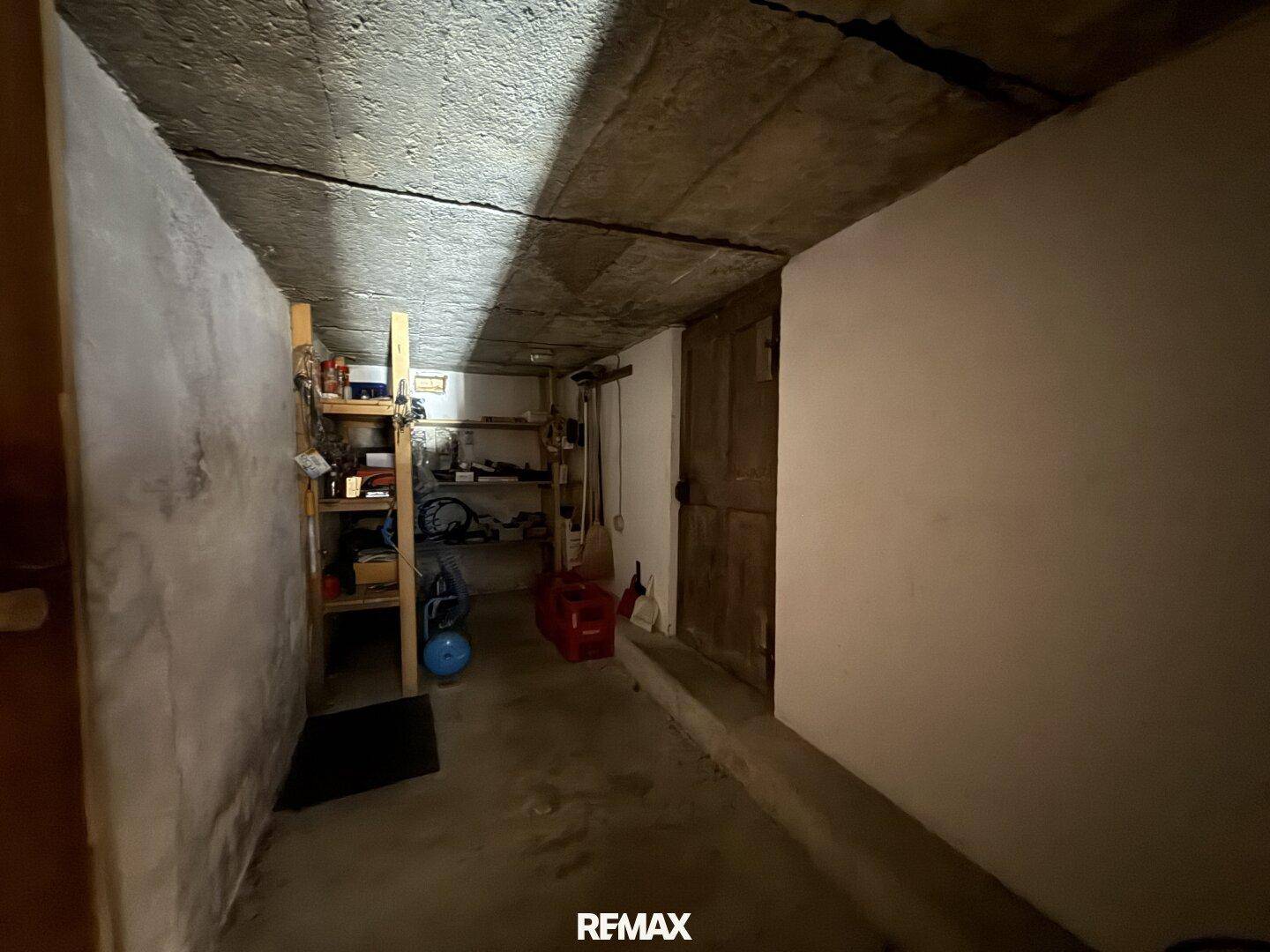 Unausgebauter Kellerraum mit Betonboden und Regalen für Lagerzwecke, einfacher Zustand.