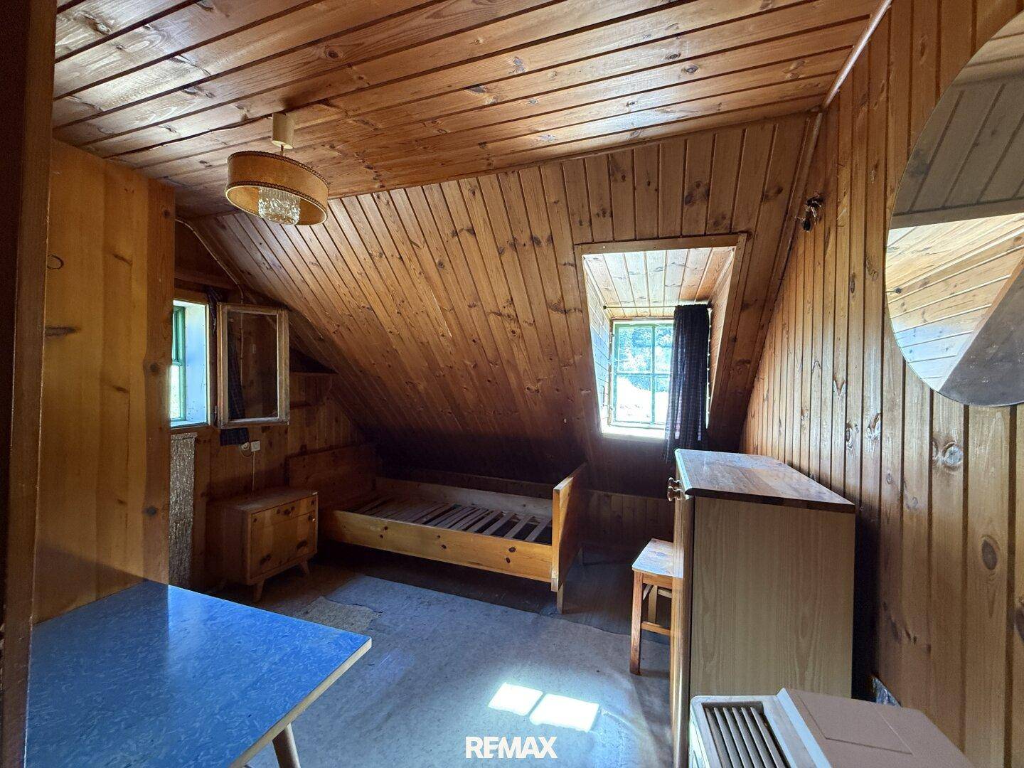Schlafzimmer im Dachgeschoss mit Holzvertäfelung, schrägen Decken und einfachem Bettgestell.