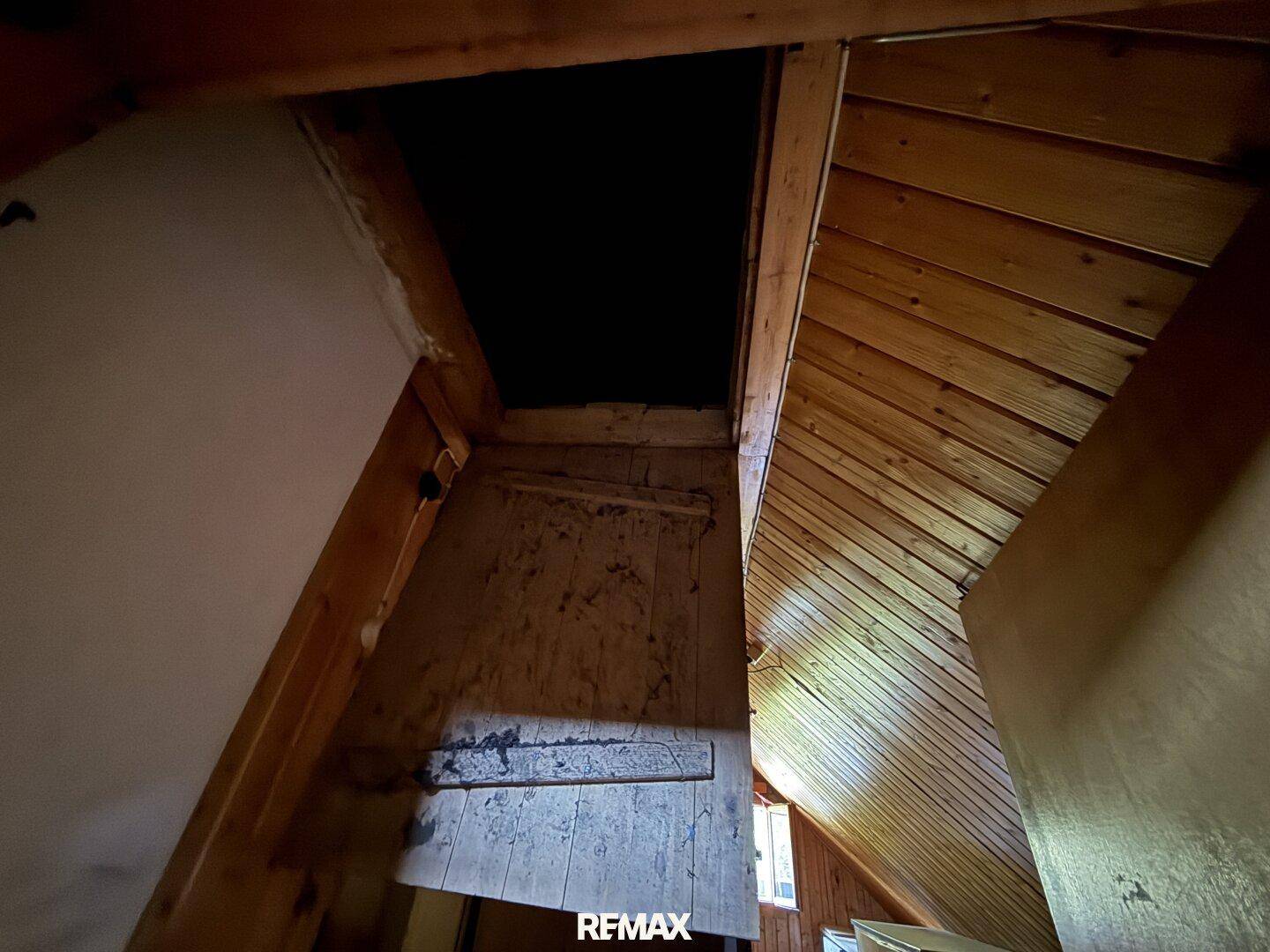 Dachbodenraum mit schrägen Holzdecken und einer dunklen Öffnung, die zu einem weiteren Bereich führt.