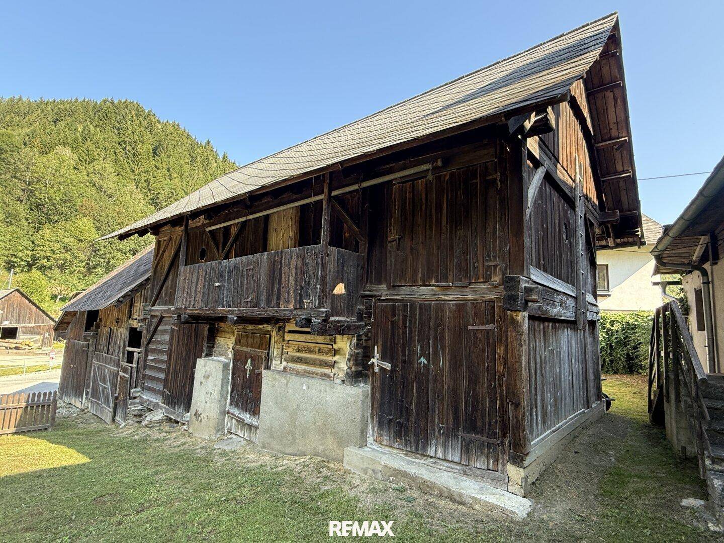 Rustikale Holzscheune mit traditioneller Bauweise und Holztüren, umgeben von grüner Wiese.