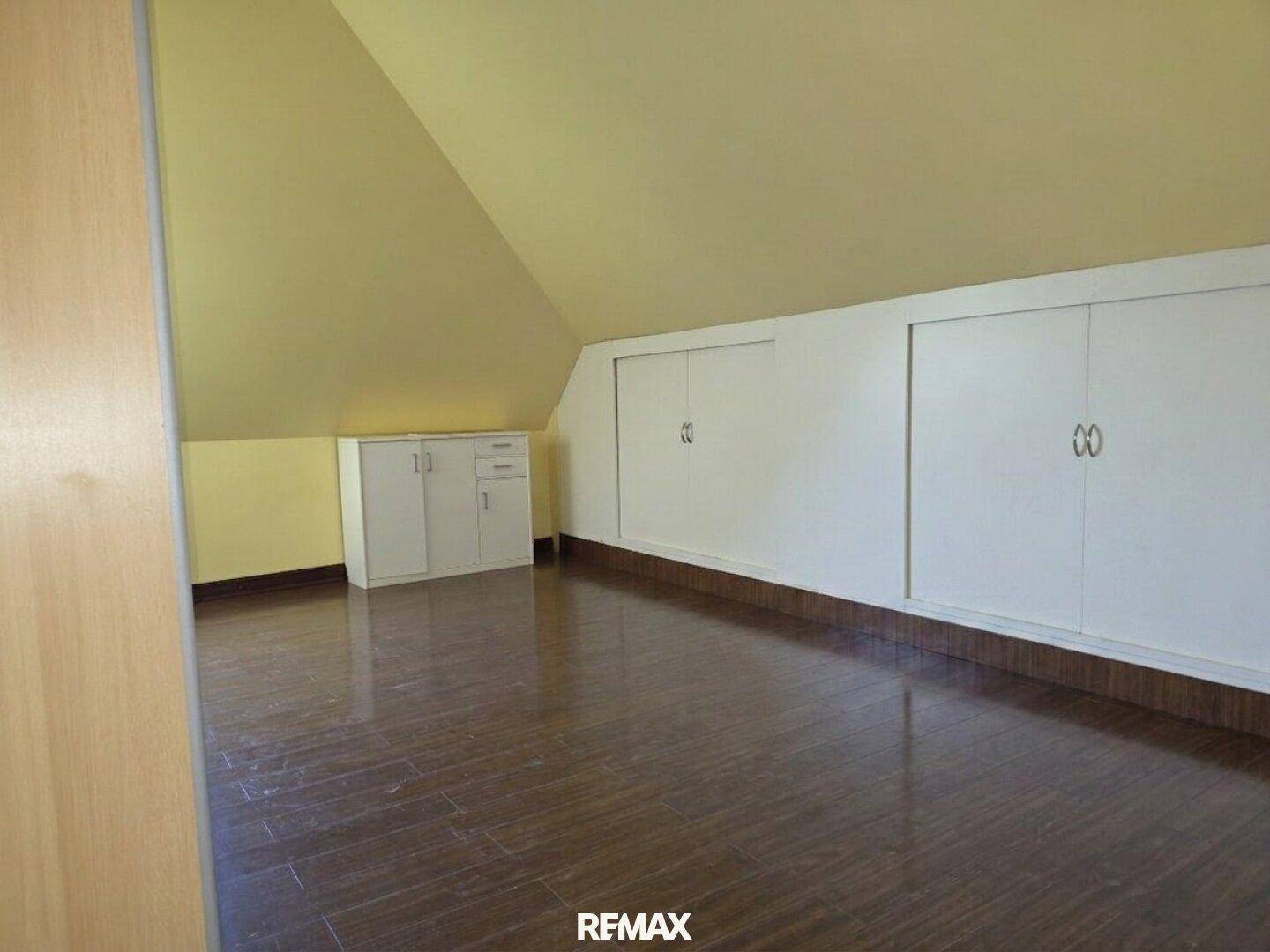 Dachzimmer mit schrägen Wänden, praktischen Einbauschränken und dunklem Holzboden.