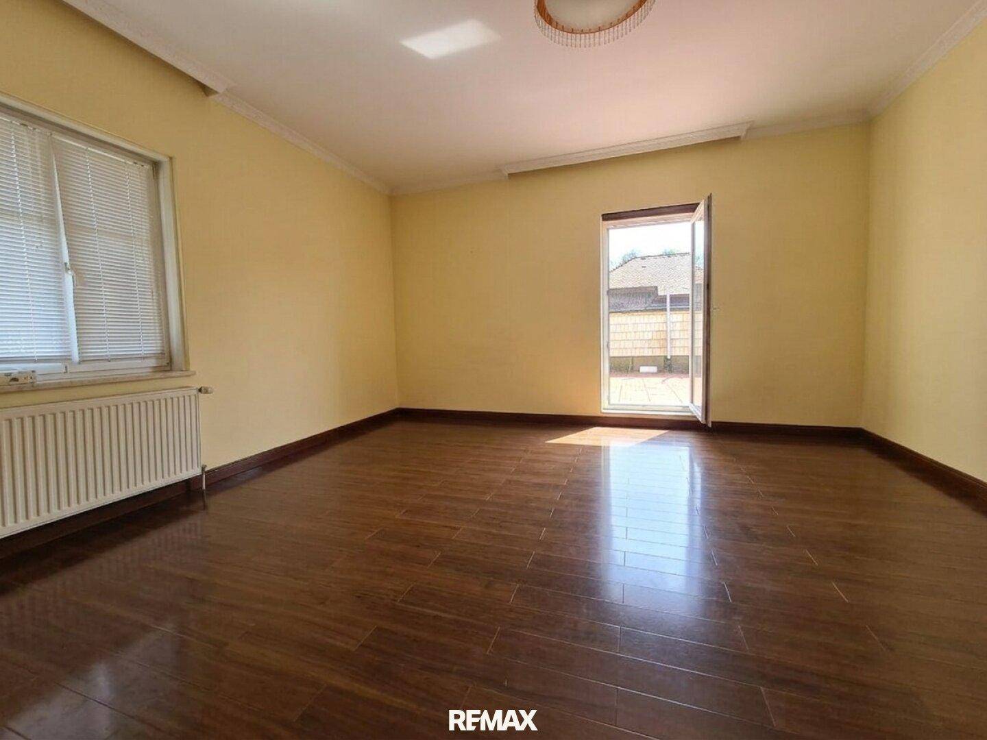 Heller, leerer Raum mit gelben Wänden, dunklem Holzboden und Zugang zu einem Außenbereich.