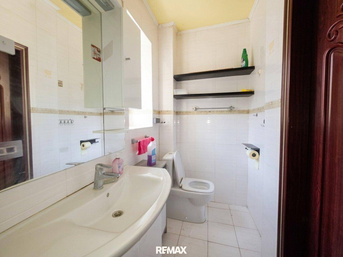 Funktionales Badezimmer mit weißen Fliesen, Einzelwaschbecken, Toilette und Spiegelschrank.