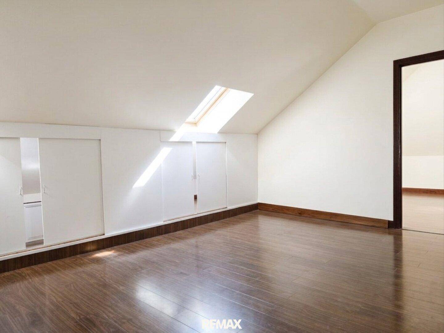 Helles Dachzimmer mit Dachfenster, Einbauschränken und dunklem Holzboden.