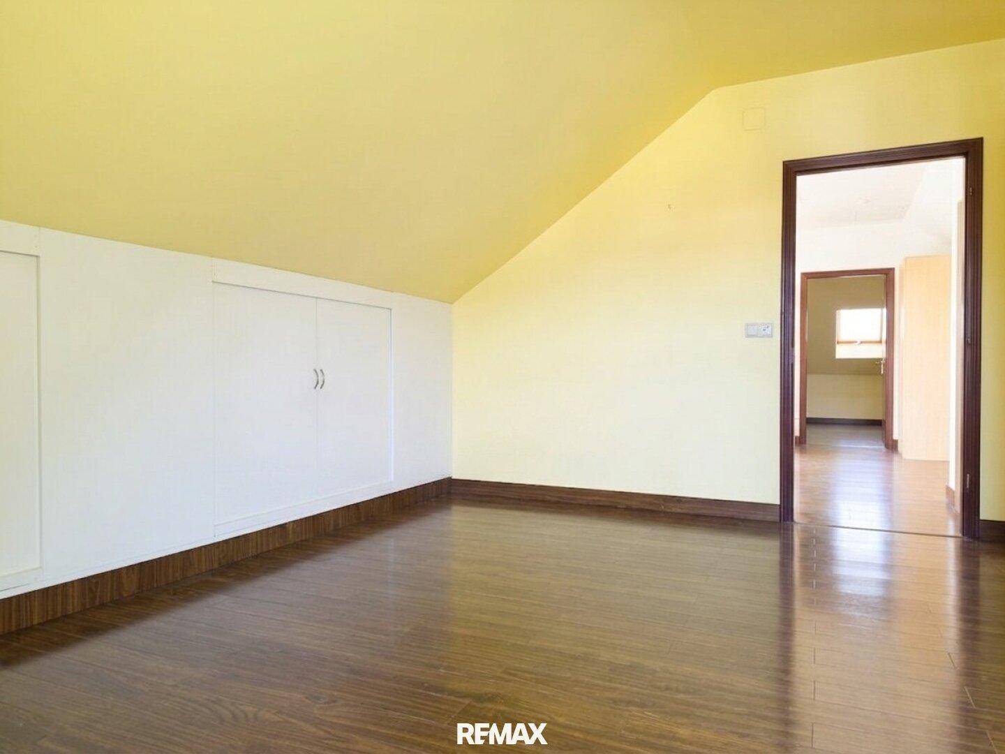 Geräumiges Dachzimmer mit schrägen Wänden, Einbauschränken und dunklem Holzboden.