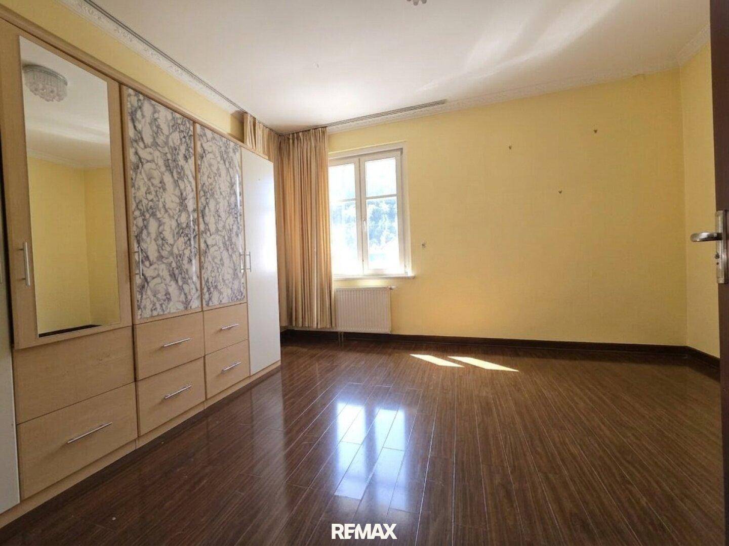 Schlafzimmer mit gelben Wänden, dunklem Holzboden und einem großen Kleiderschrank mit Spiegeltüren.