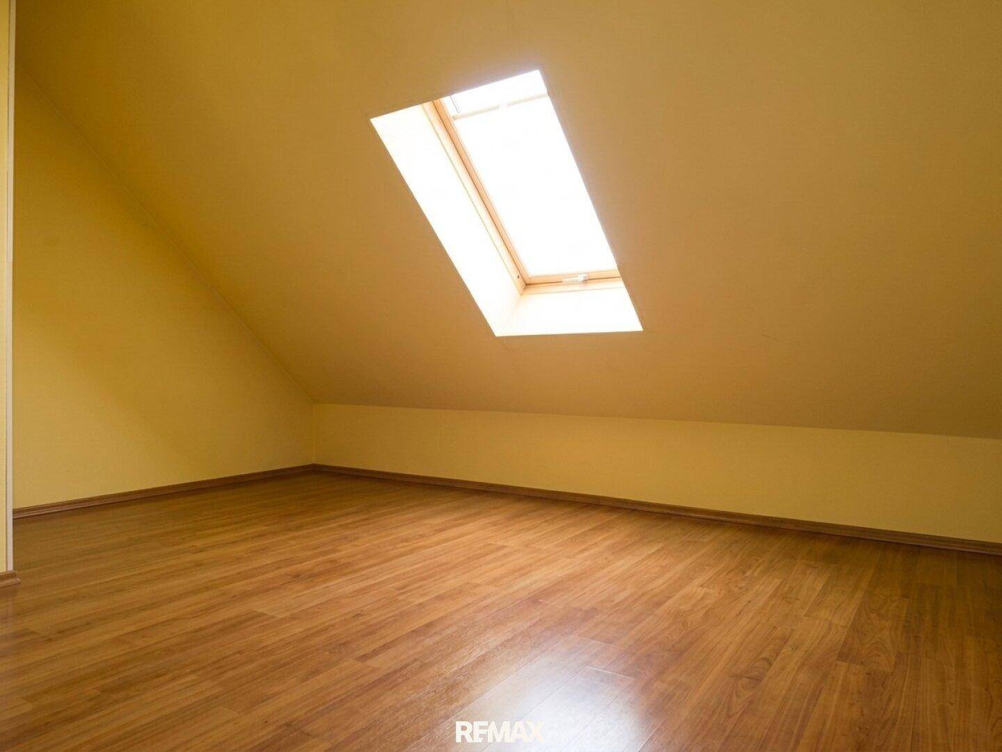 Dachzimmer mit einem großen Dachfenster, das viel natürliches Licht hereinlässt, und dunklem Holzboden.