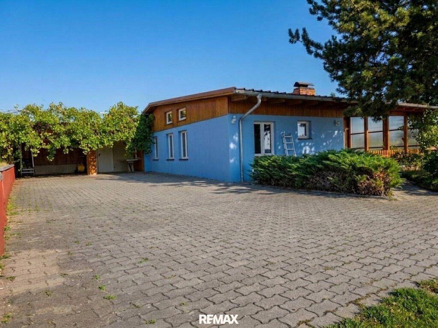 Seitenansicht des blauen Hauses mit großem gepflasterten Hof und Carport.