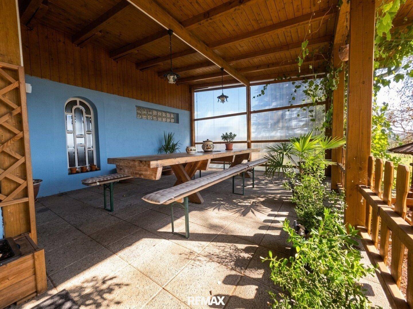 Überdachte Terrasse mit großem Holztisch und Bänken, ideal für Mahlzeiten im Freien.