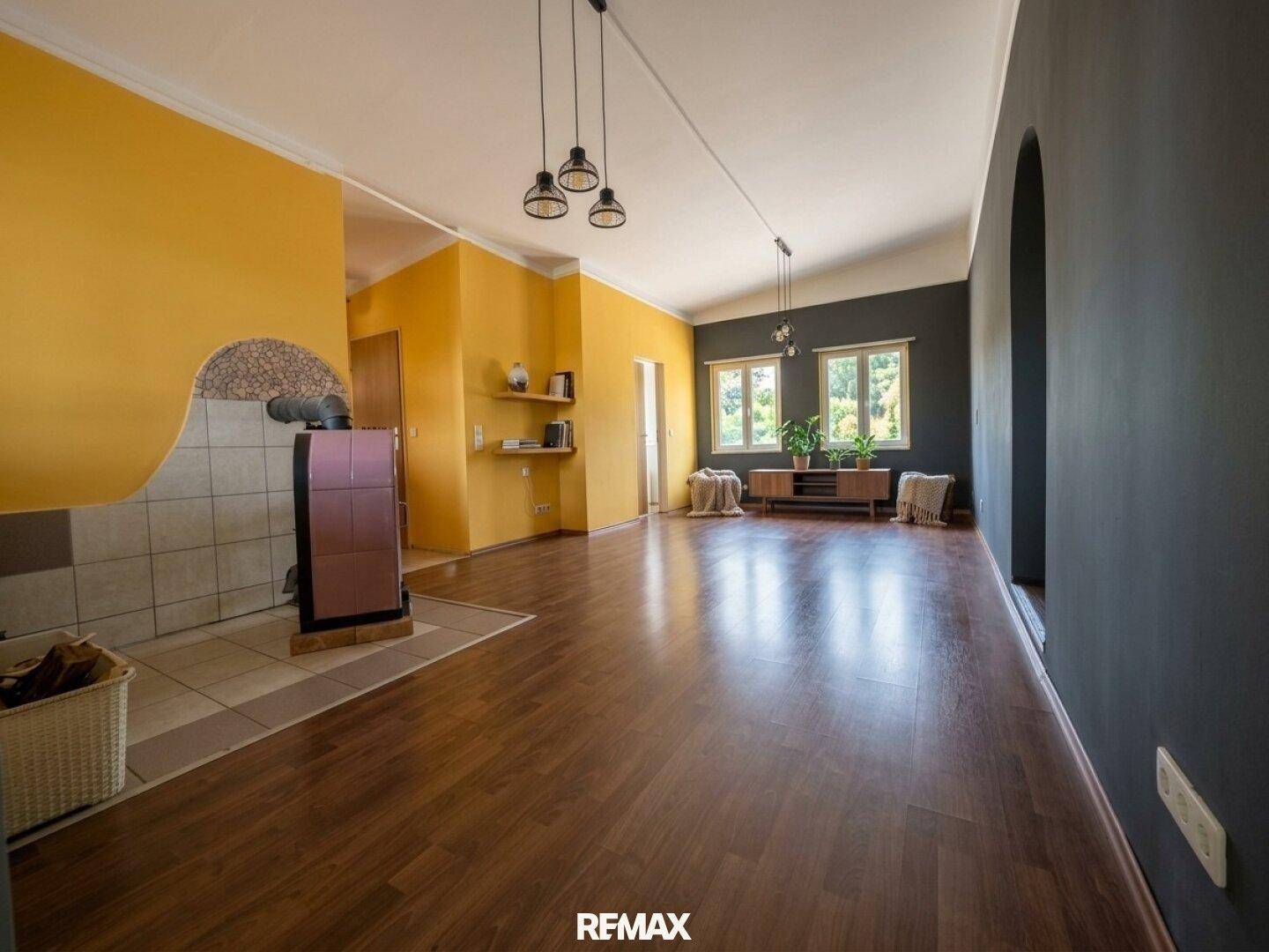 Geräumiges Wohnzimmer mit Holzboden, Kaminofen und farbigen Wänden in Gelb und Grau.