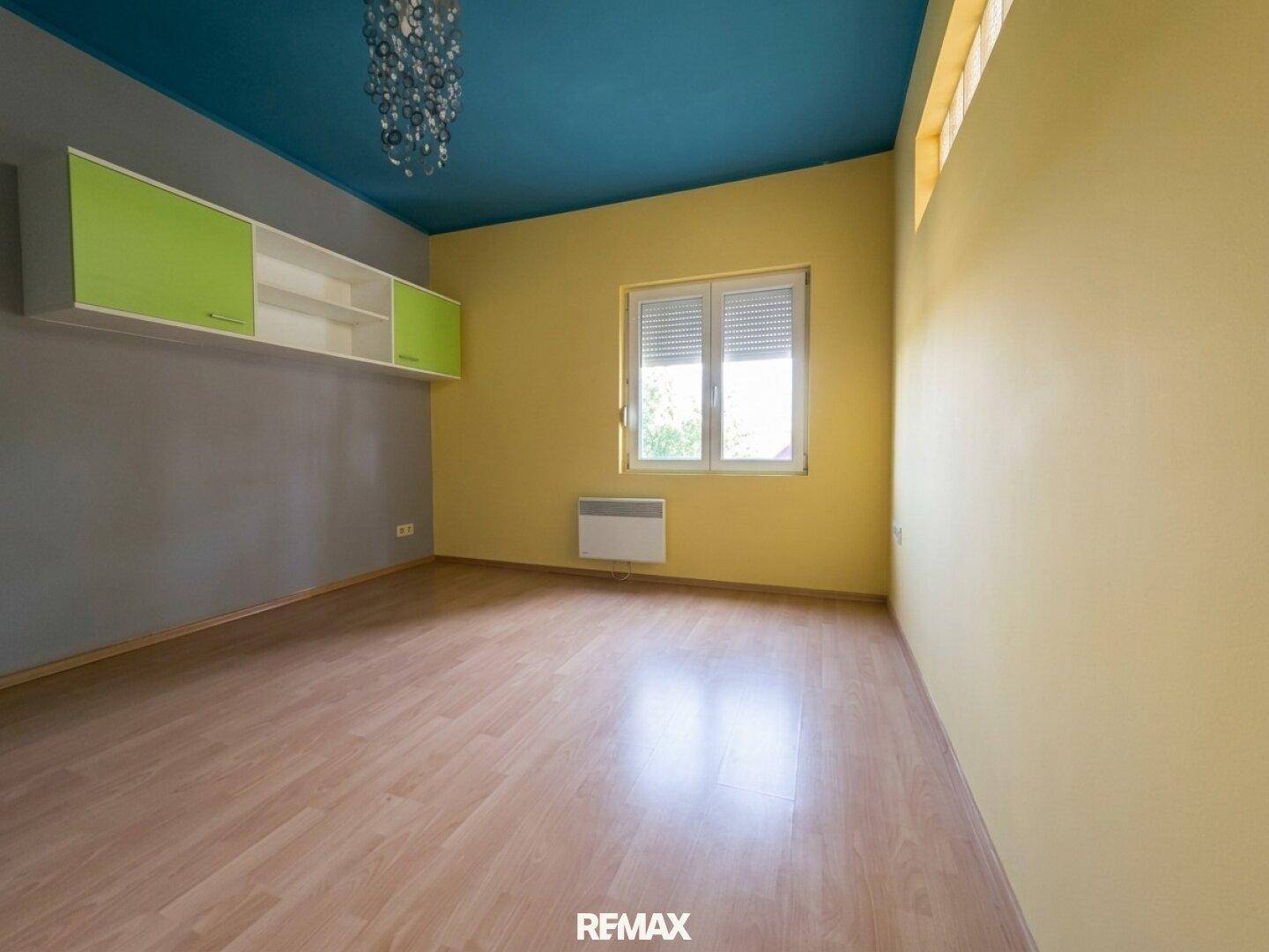 Schlafzimmer mit Laminatboden, farbigen Wänden und Rollläden am Fenster.