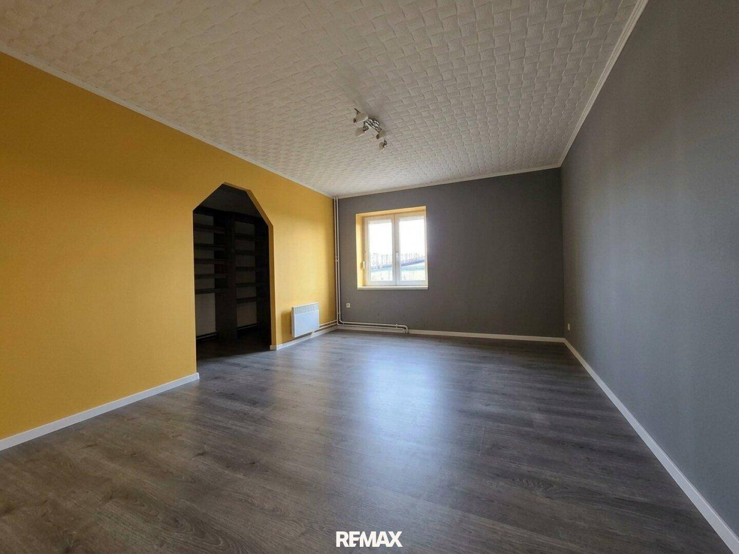 Geräumiges Wohnzimmer mit Laminatboden und farbigen Wänden in Gelb und Grau.