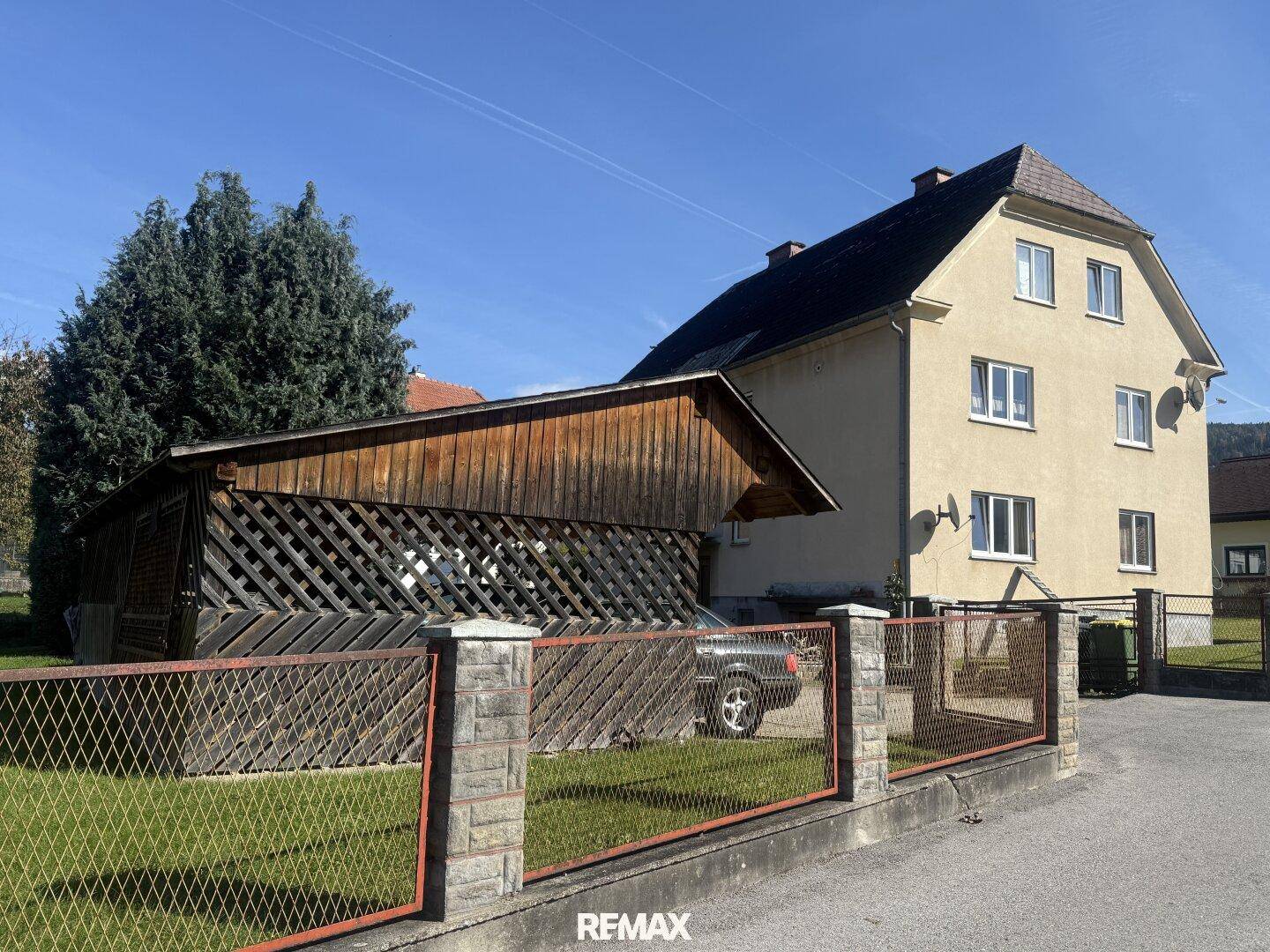 Rückansicht des Hauses mit Holzschuppen und Zaun, umgeben von Grünflächen.