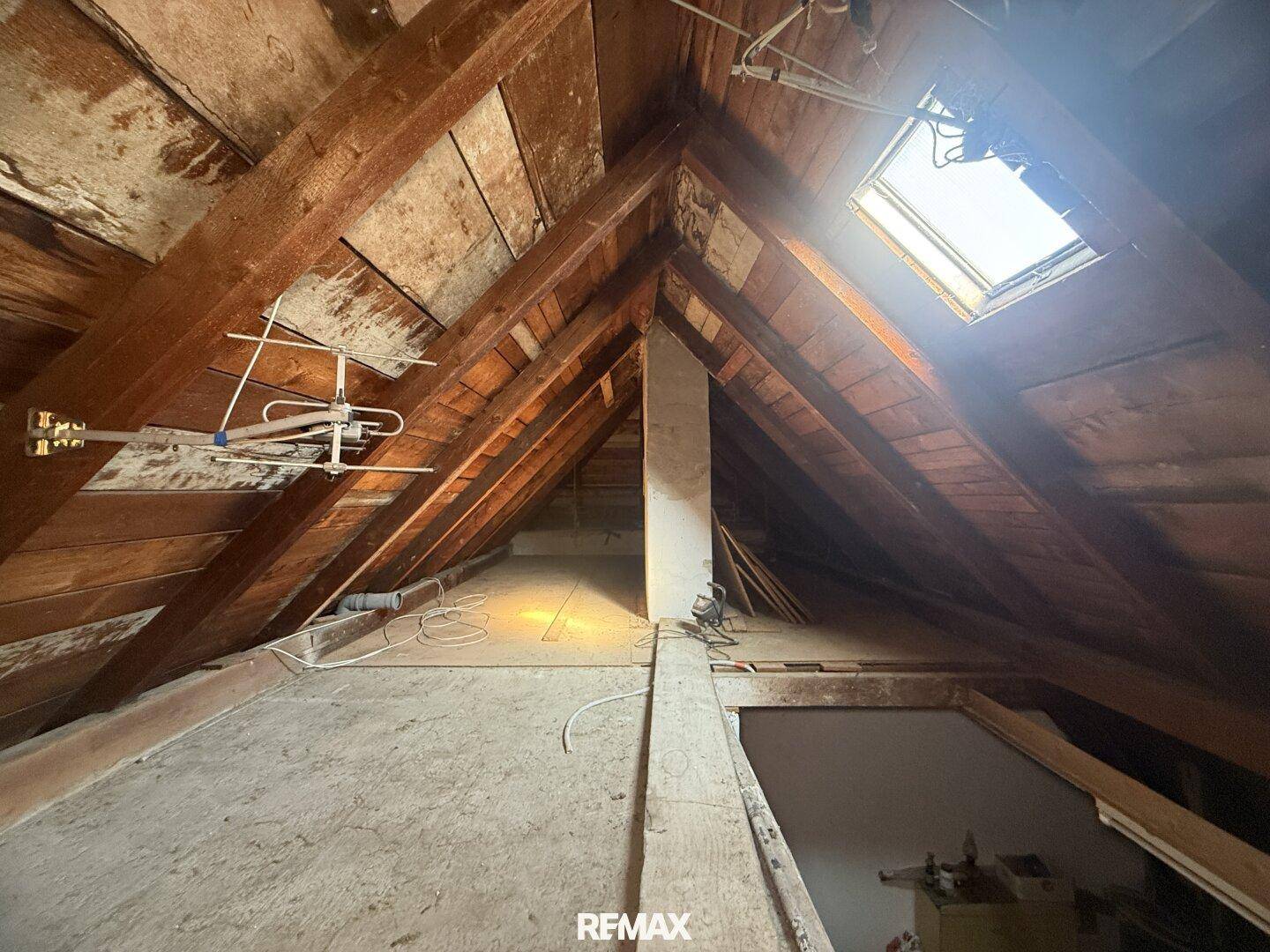 Unausgebauter Dachboden mit sichtbaren Holzbalken und Dachfenster, bietet Ausbaupotenzial.