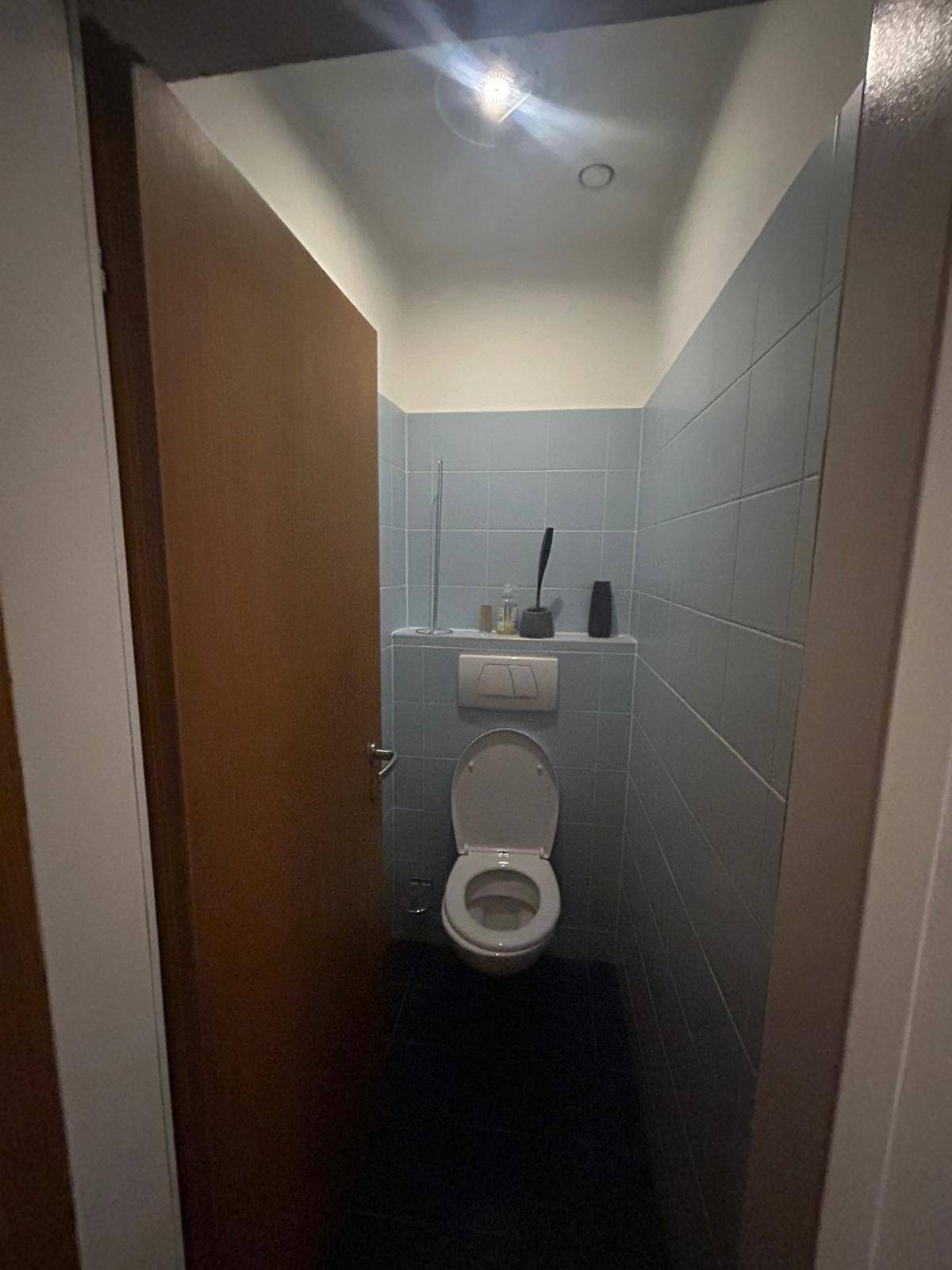 Kleines WC mit Toilette und blauen Wandfliesen, funktional und einfach gestaltet.