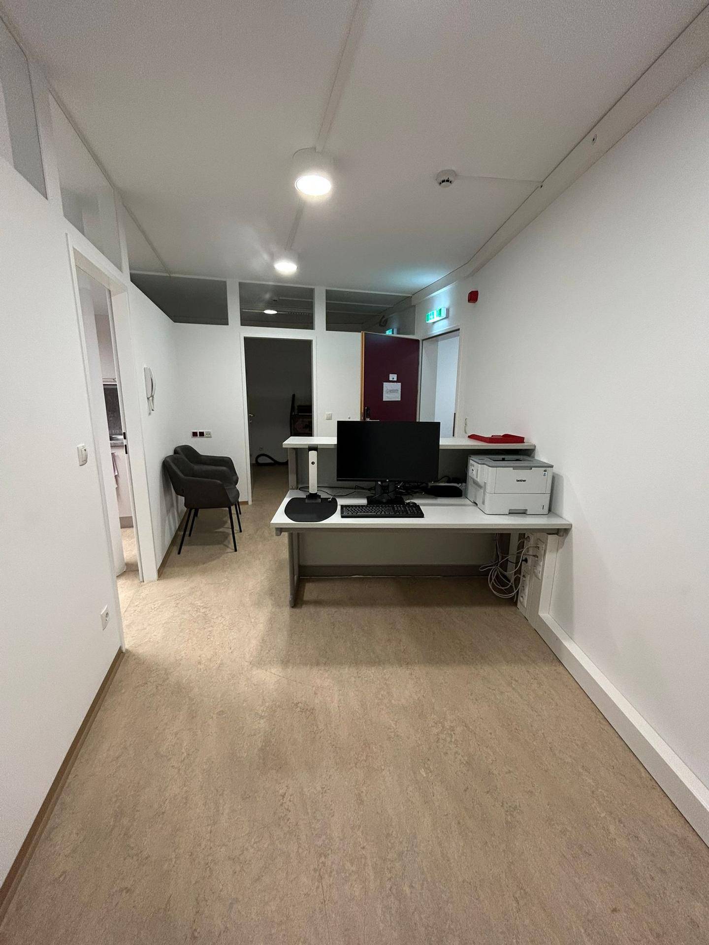 Funktionaler Büroarbeitsplatz mit Computer und Drucker, der einen Blick in den Empfangsbereich ermöglicht.