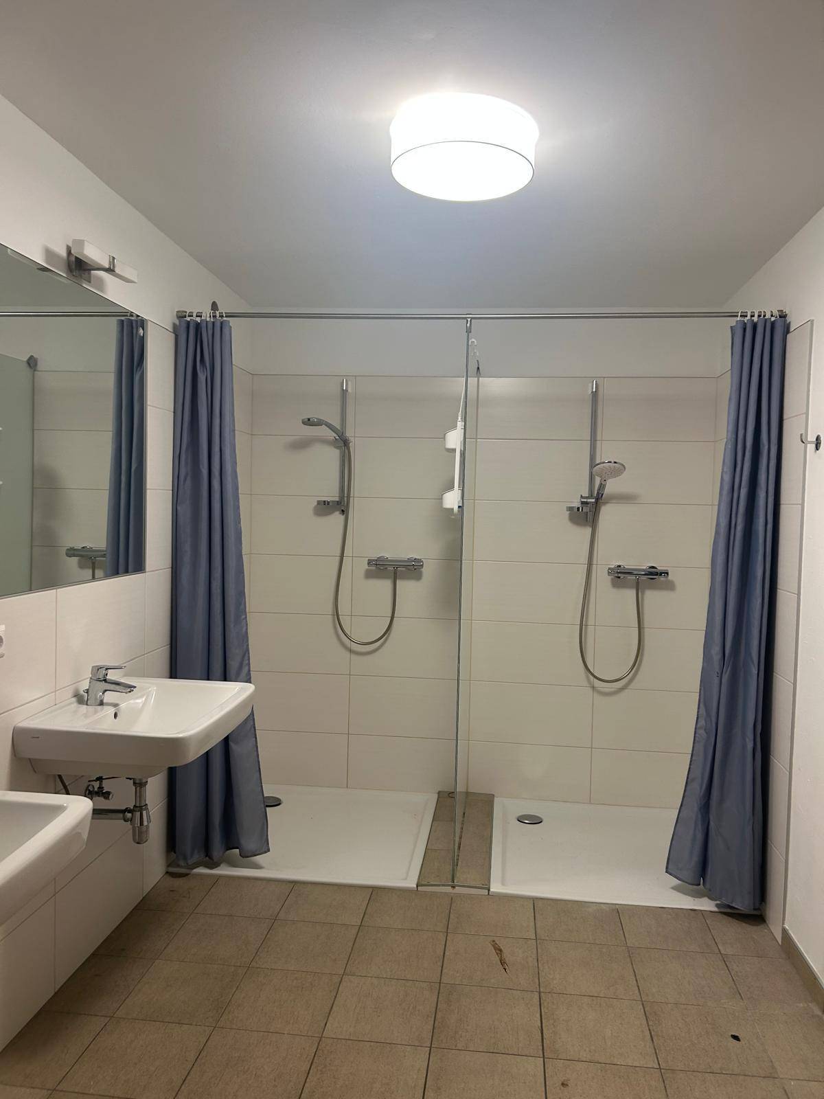 Funktionales Badezimmer mit zwei Duschkabinen, zwei Waschbecken und hellen Fliesen, ideal für mehrere Nutzer.