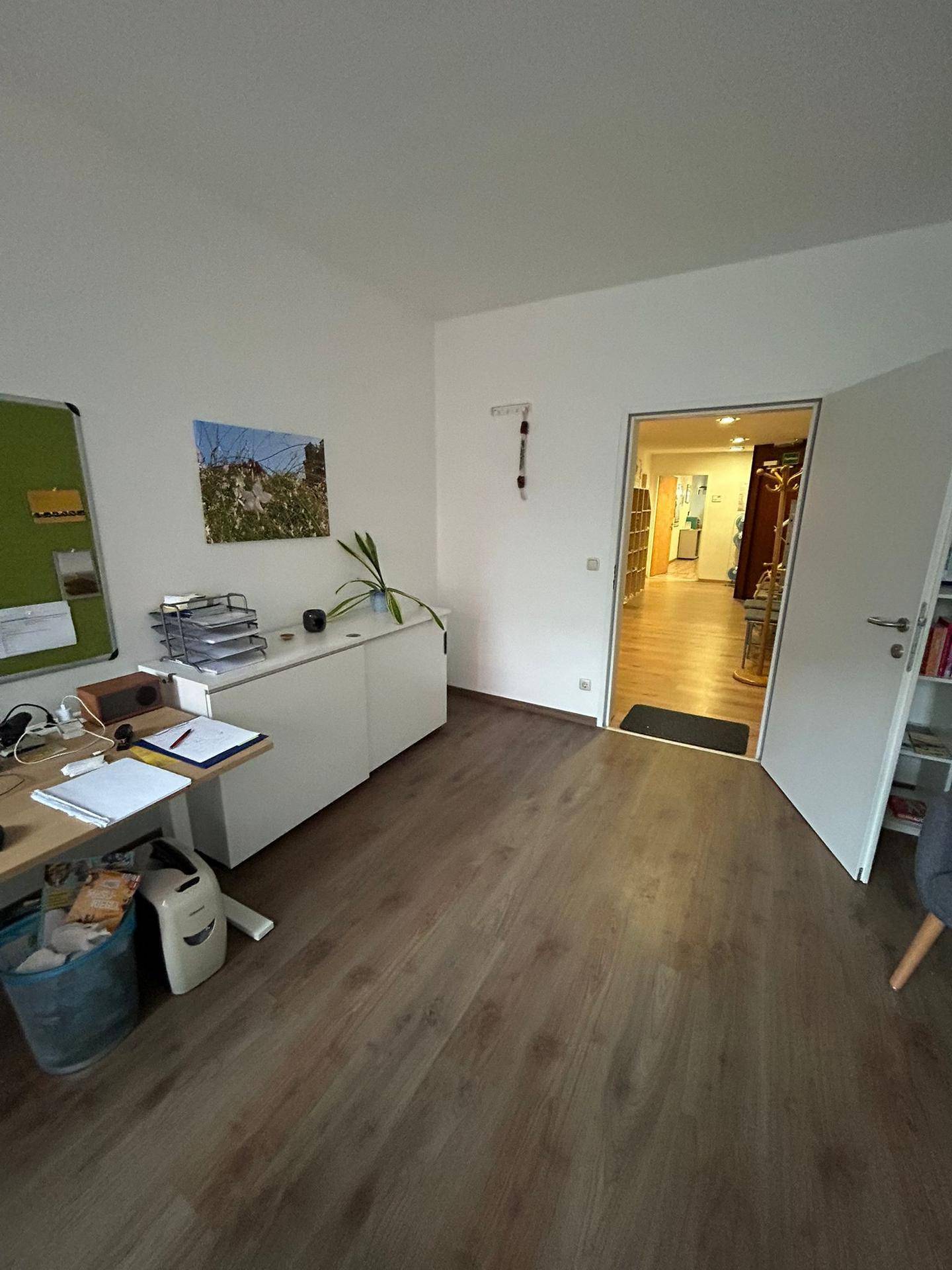 Büro mit hellem Laminatboden, weißem Sideboard und offener Tür zu einem angrenzenden Flur.