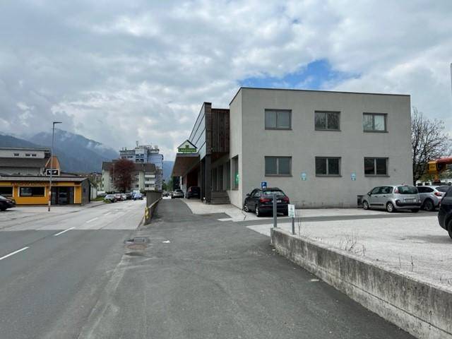 Ansicht des Geschäftsgebäudes von der Straße mit Parkplätzen und Bergen im Hintergrund.