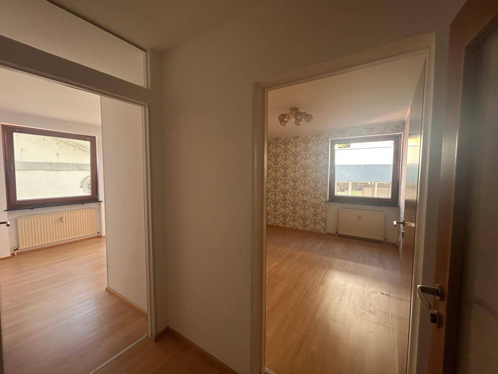 Flur mit Laminatboden und Zugang zu zwei Zimmern, eines davon mit gemusterter Tapete und Fenster.