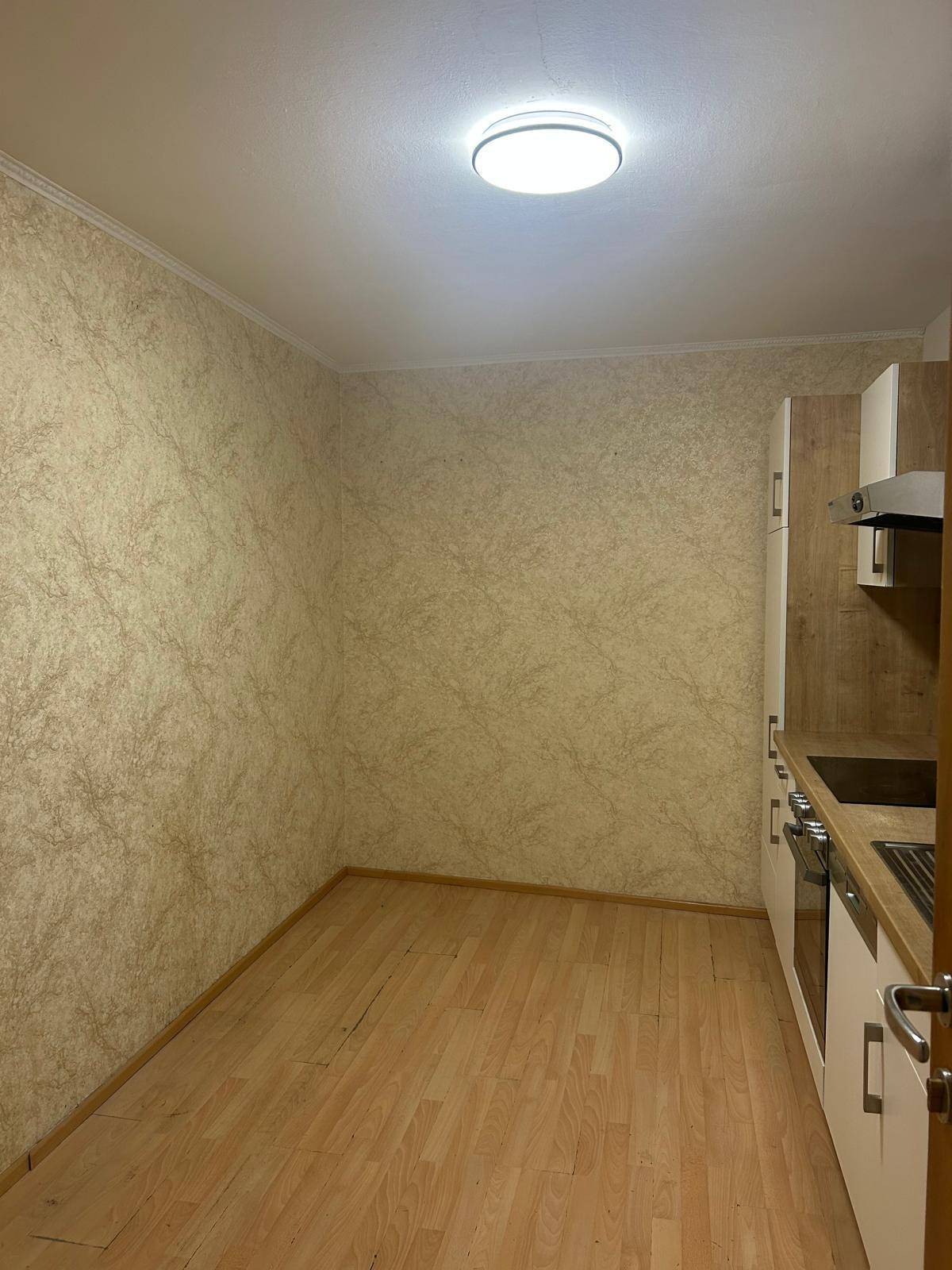 Geräumiger Küchenbereich mit heller Küchenzeile, Laminatboden und gemusterter Tapete, bereit zur individuellen Gestaltung.