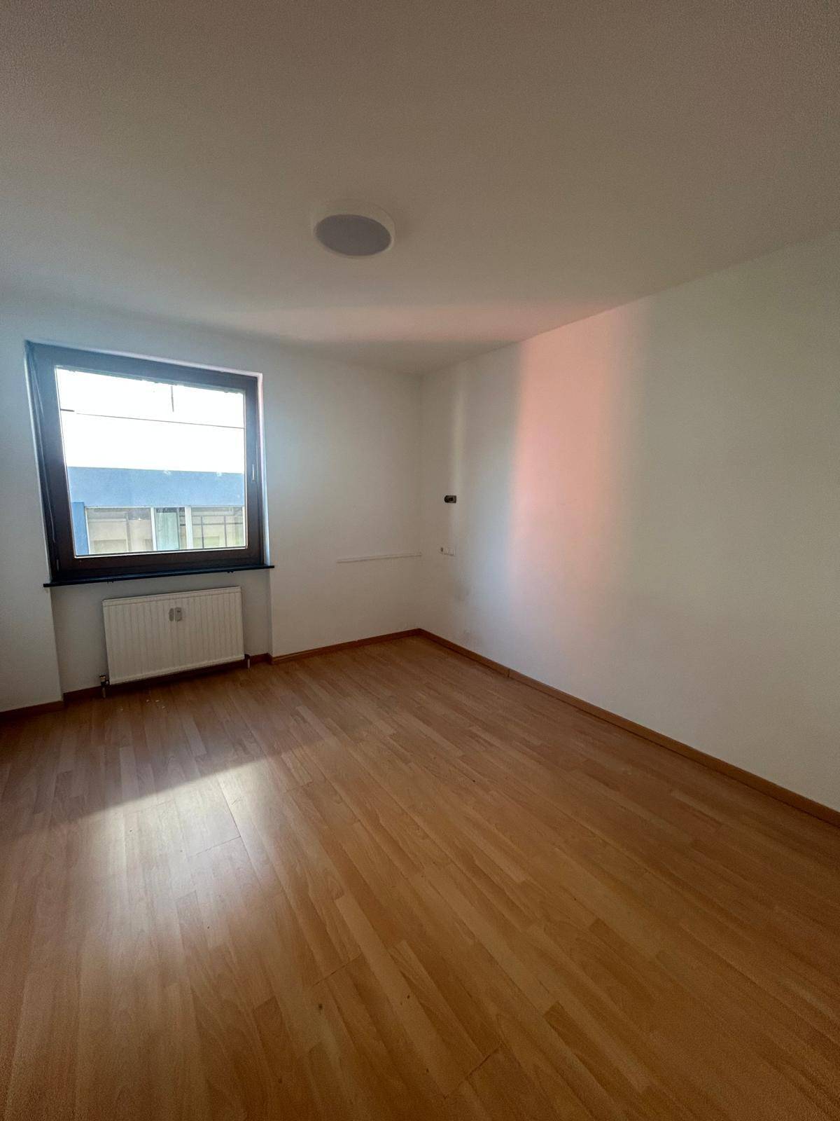 Heller Raum mit Laminatboden, weißen Wänden und einem Fenster, das viel natürliches Licht spendet.
