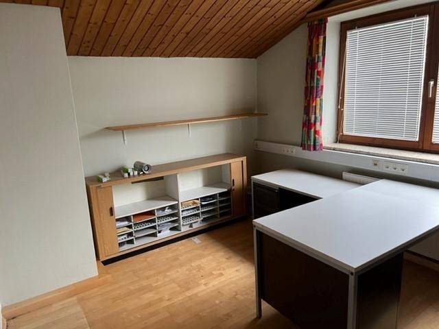 Büro mit Holzboden, Dachschräge und funktionalen Möbeln, gut beleuchtet durch ein Fenster.