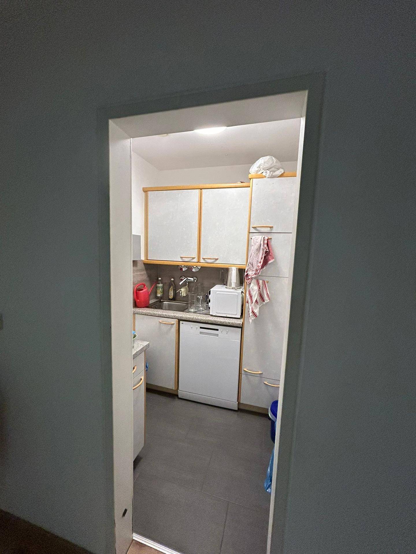 Kleine Küchenzeile mit weißen Schränken, Spüle, Geschirrspüler und dunklem Fliesenboden.