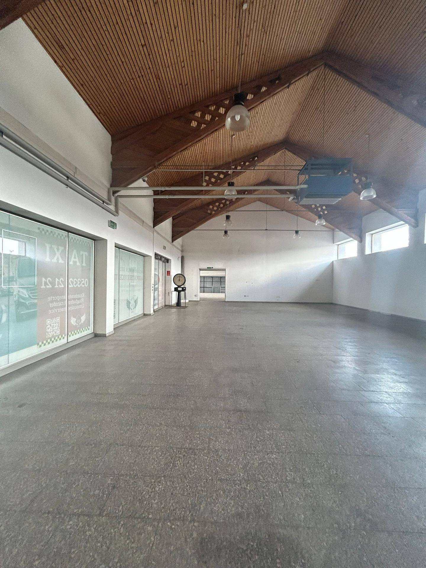 Weitläufiger, leerer Gewerberaum mit Holzdachkonstruktion und großen Schaufenstern.