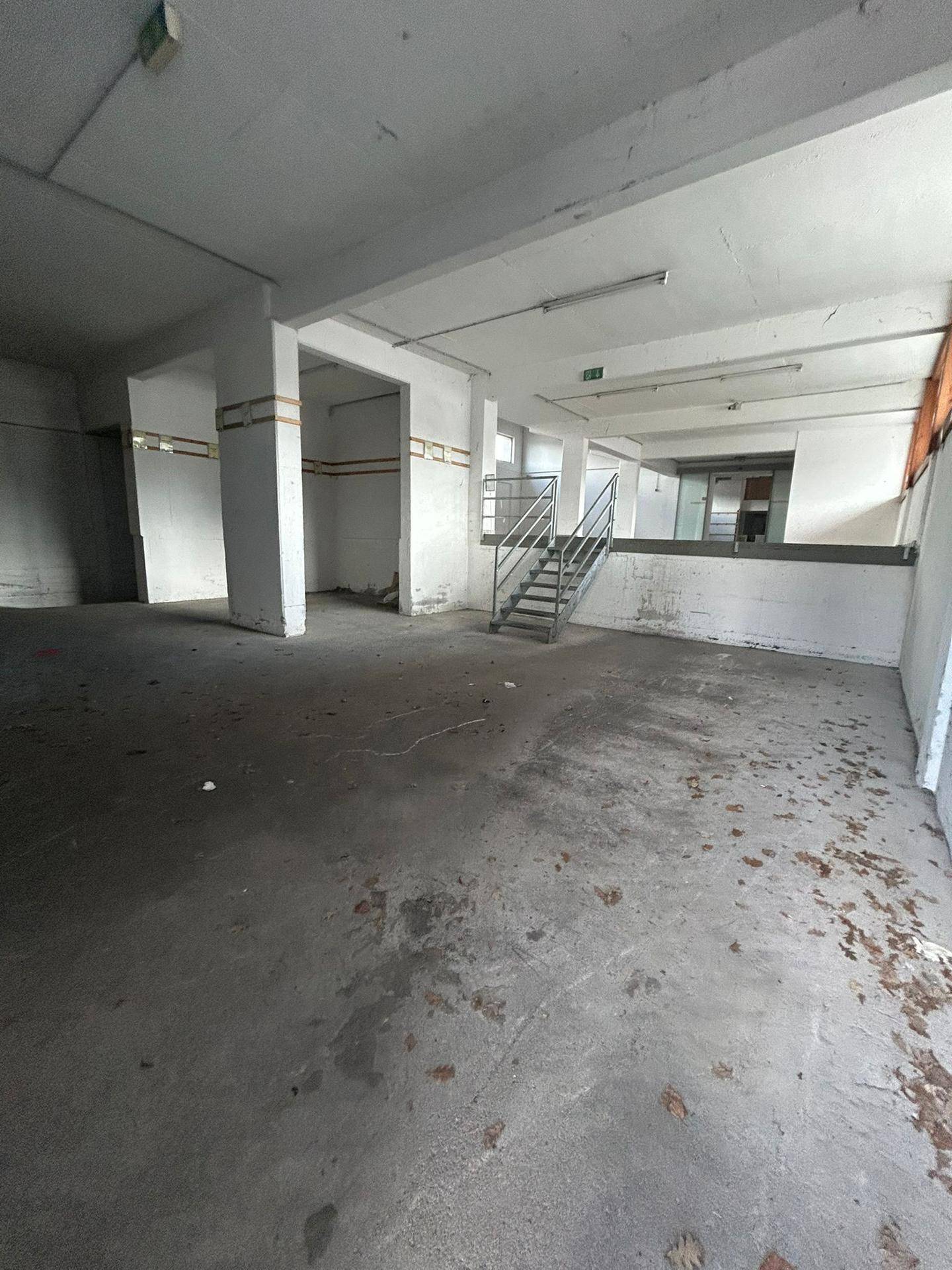 Großer, leerer Gewerberaum mit Betonboden, Säulen und Treppenaufgang, vielseitig nutzbar.