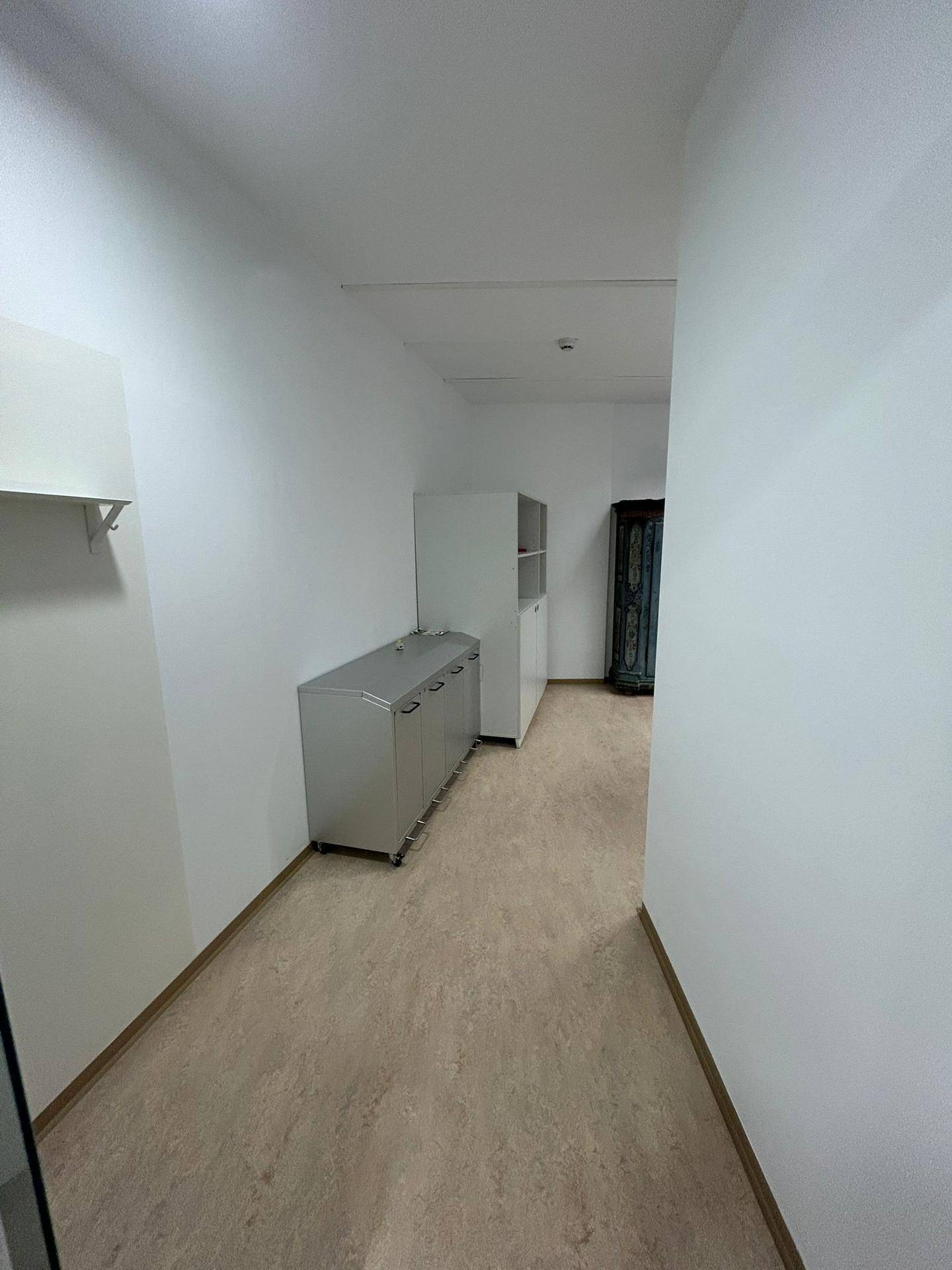 Langer, heller Flur mit modernem Bodenbelag und verschiedenen Büromöbeln entlang der Wand, gut organisiert.
