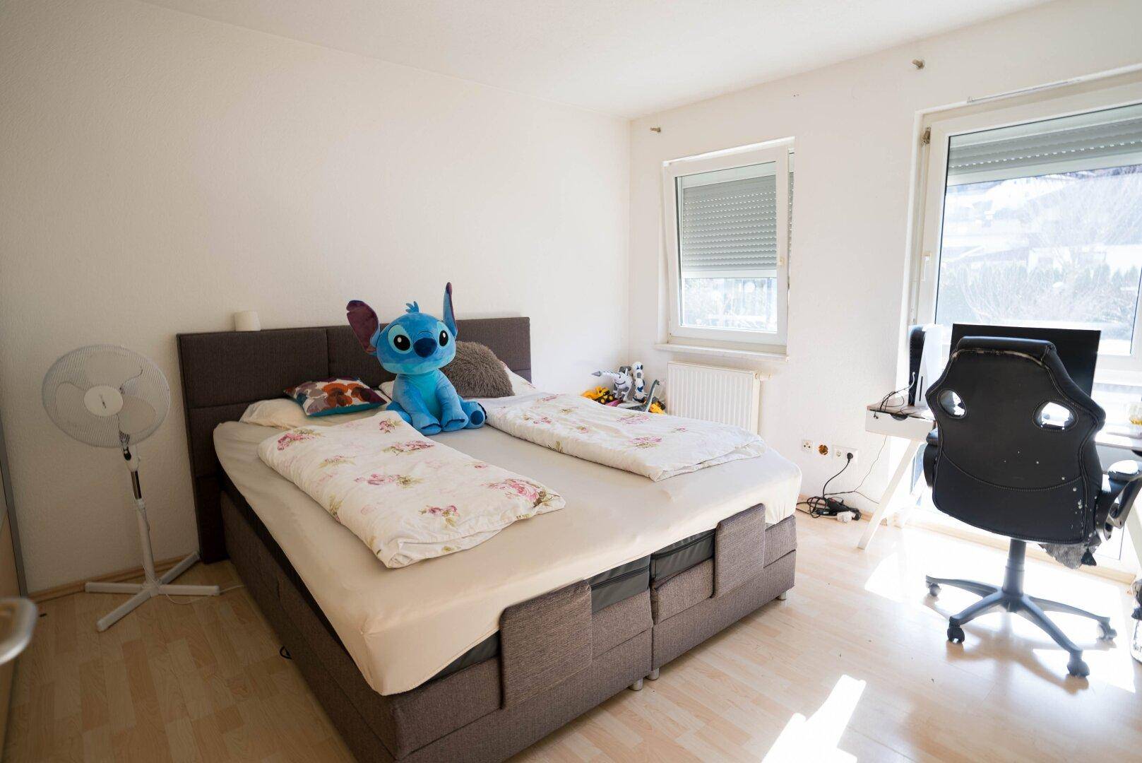 Helles Schlafzimmer mit Doppelbett, Schreibtisch und Laminatboden.