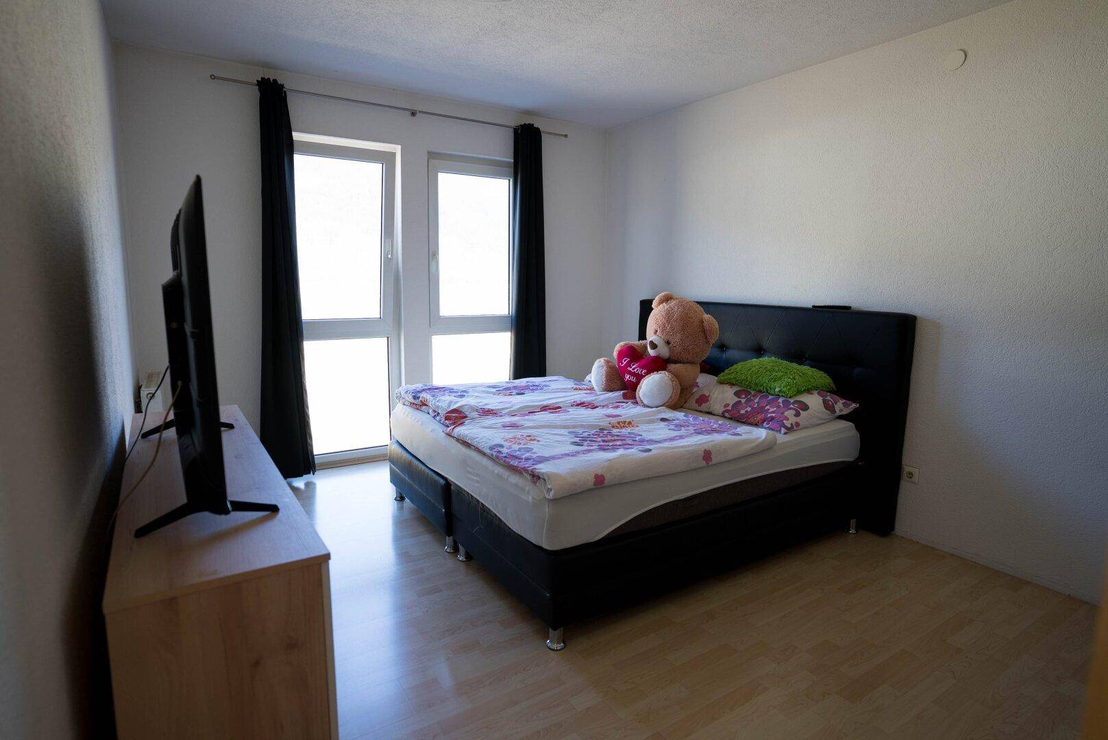 Schlafzimmer mit Doppelbett, Fernseher und Zugang zu einem Fenster mit Blick ins Grüne.