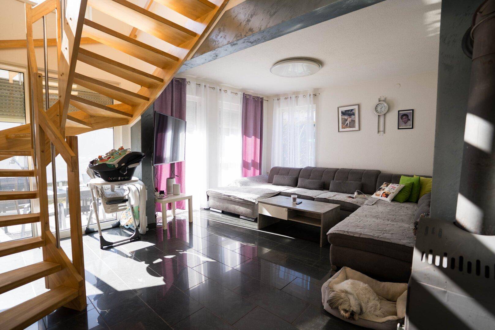 Helles Wohnzimmer mit dunklen Fliesen, gemütlichem Sofa und eleganter Holztreppe.