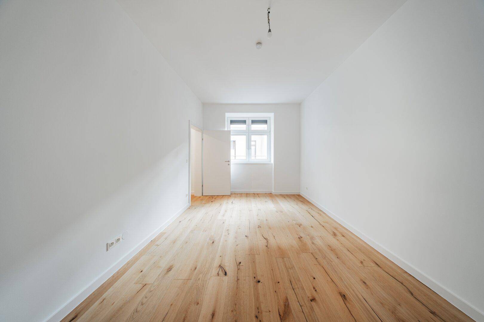 Heller, leerer Raum mit Holzboden und weiß gestrichenen Wänden, bereit zur individuellen Gestaltung.
