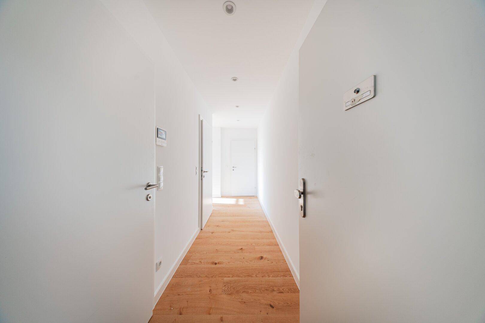 Heller und minimalistischer Flur mit Holzboden und weißen Wänden, der zu weiteren Räumen führt.