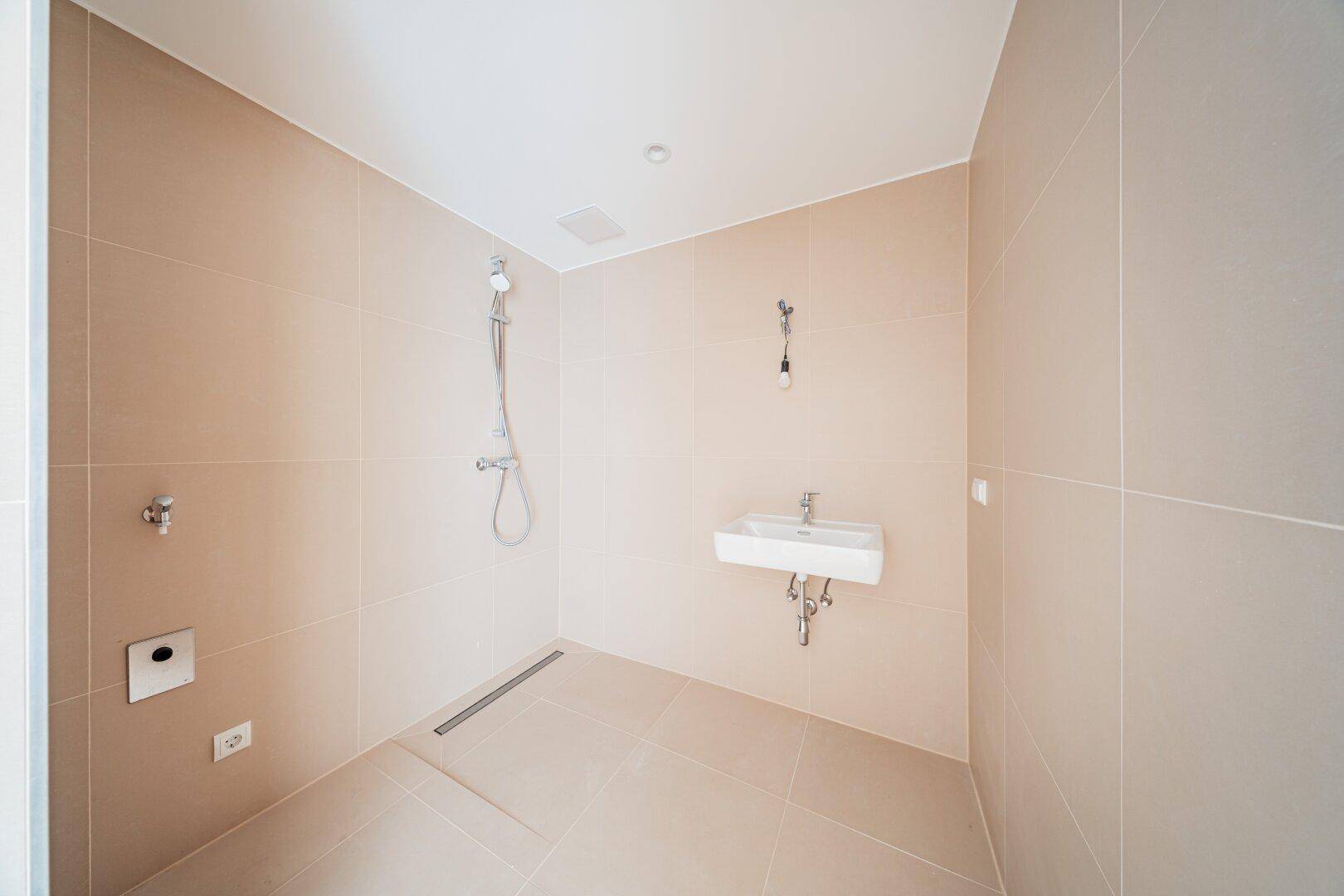 Modernes Duschbad mit ebenerdiger Dusche und Waschbecken, ideal für Barrierefreiheit.