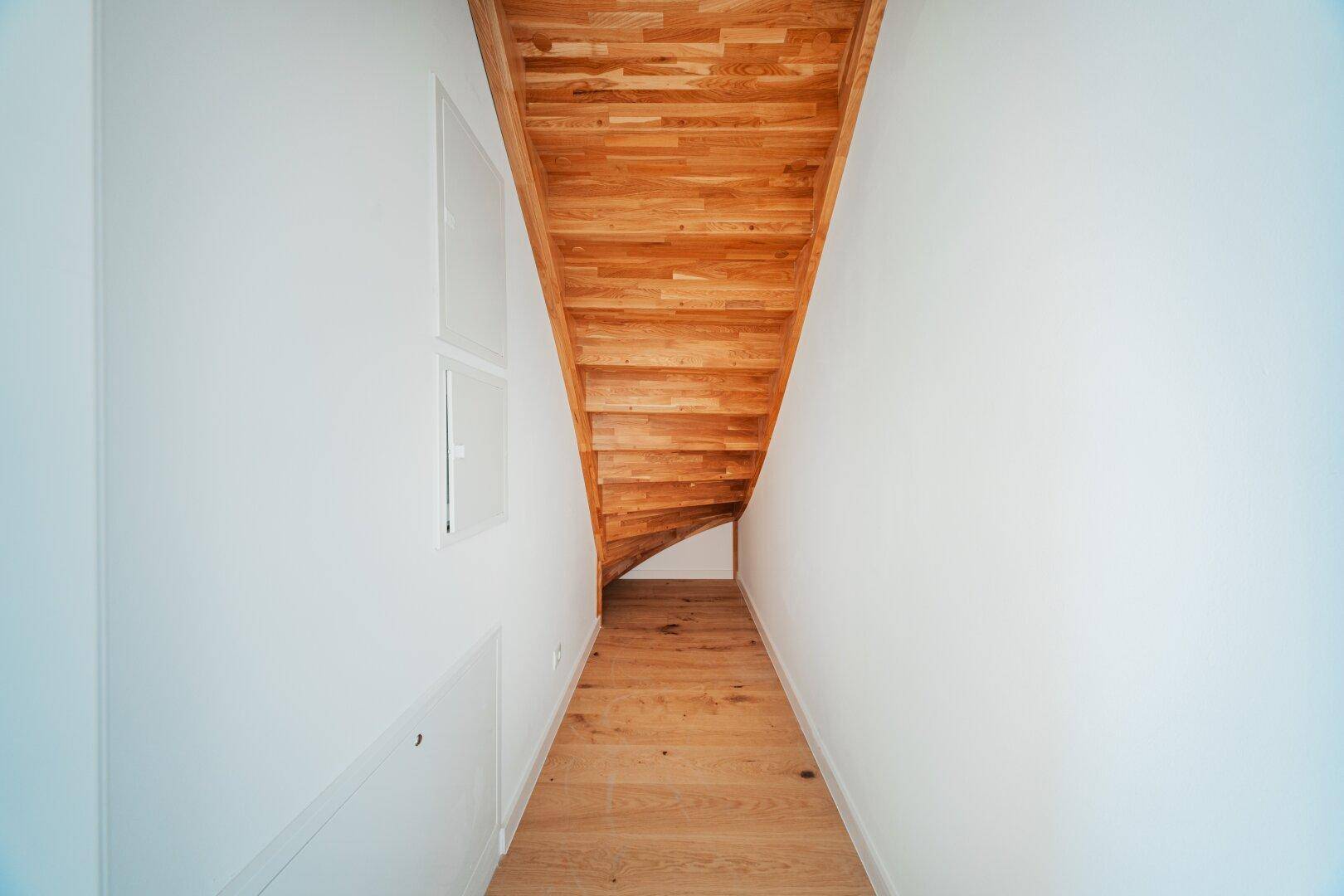 Helle Holztreppe mit weißen Wänden, die die verschiedenen Ebenen der Wohnung verbindet.