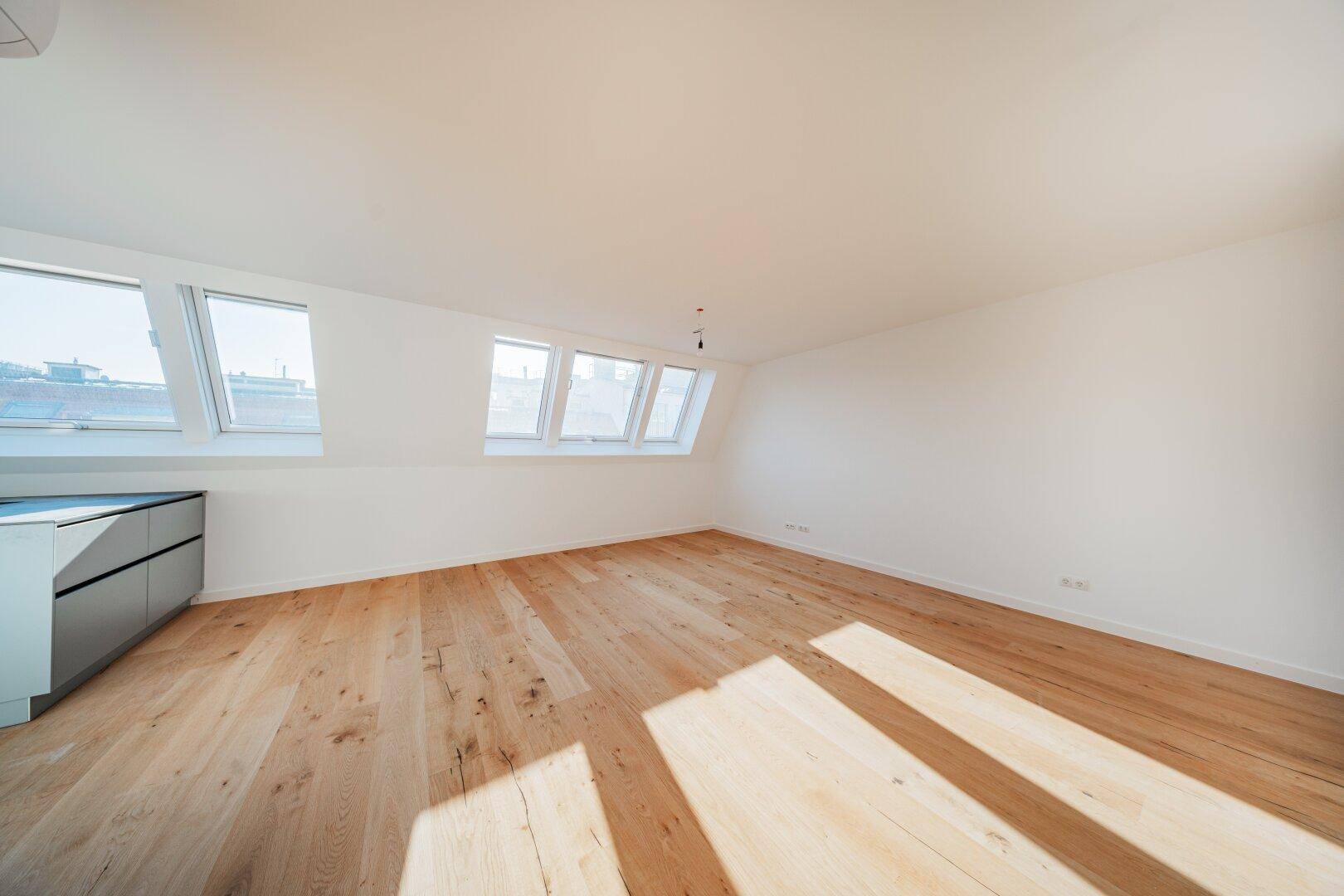 Leerer Raum im Dachgeschoss mit Holzboden und mehreren Dachfenstern, die viel Licht hereinlassen.