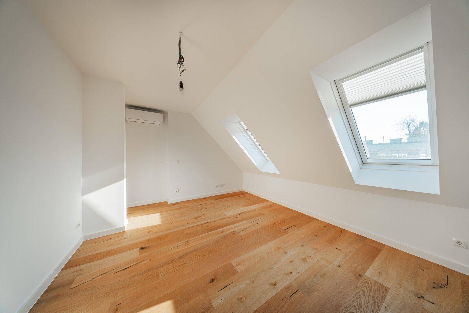 Heller Dachgeschossraum mit Holzboden, Klimaanlage und einem Dachfenster für natürliches Licht.