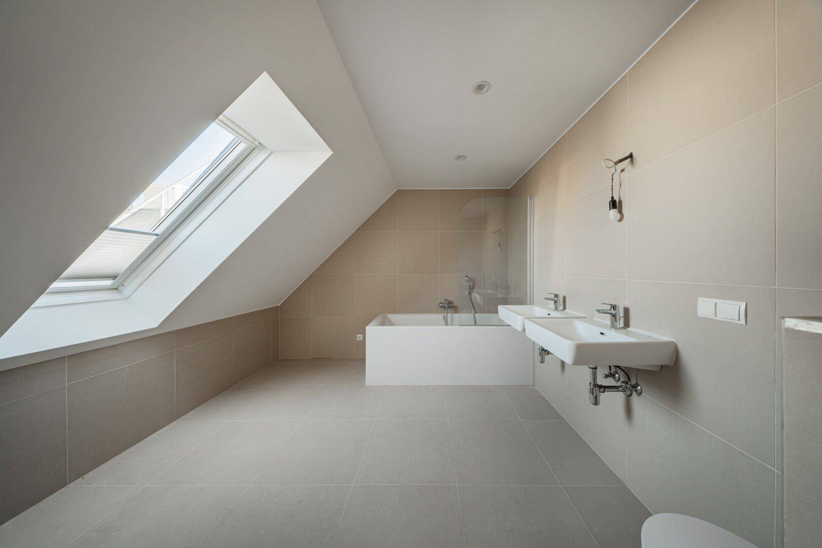 Modernes Badezimmer im Dachgeschoss mit Badewanne, Doppelwaschbecken und Dachfenster.