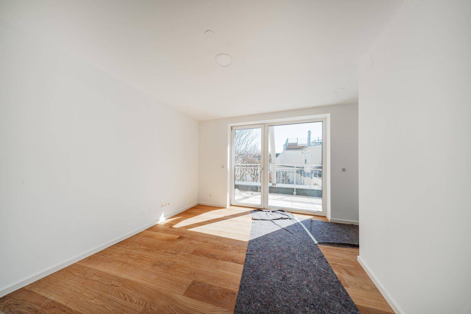 Sonniger, leerer Raum mit Holzboden und Zugang zu einem Balkon, ideal als Schlafzimmer.