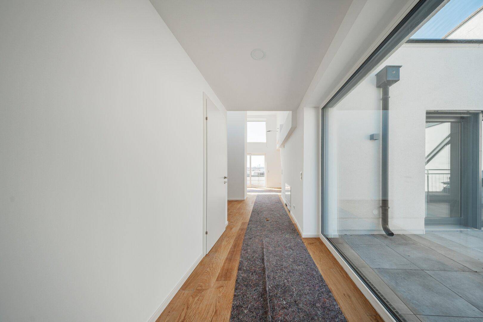 Heller Flur mit Holzboden und großer Fensterfront, die viel Tageslicht hereinlässt.