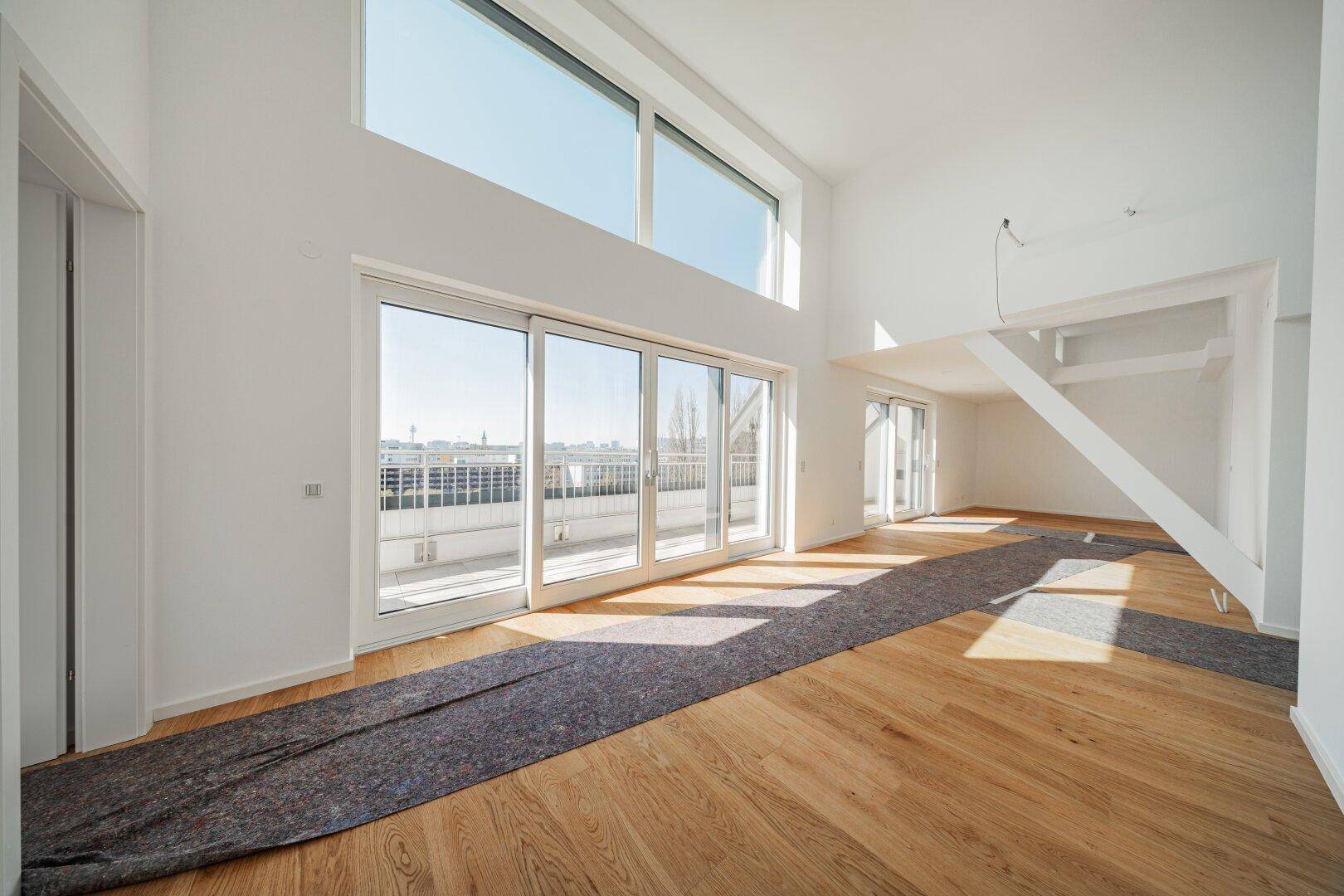 Geräumiges, lichtdurchflutetes Wohnzimmer mit hohen Decken und Holzboden, bereit zur Einrichtung.