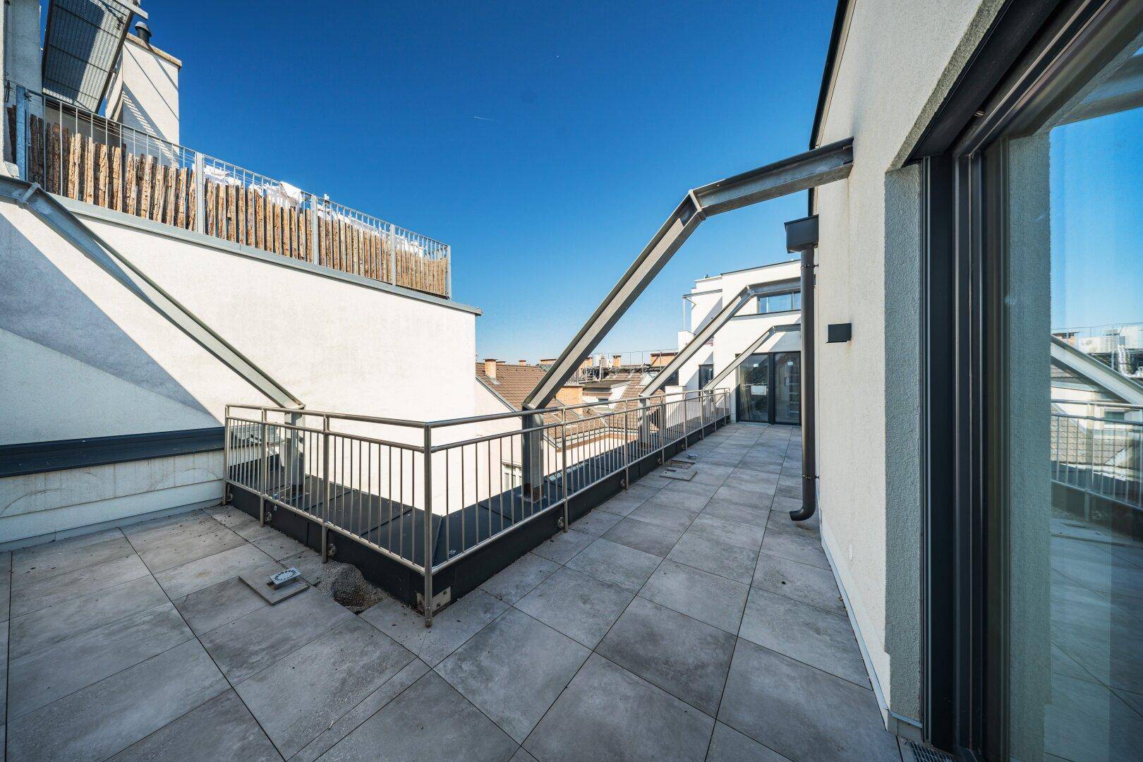 Weitläufige Dachterrasse mit Fliesenboden und modernem Metallgeländer, ideal zum Entspannen.