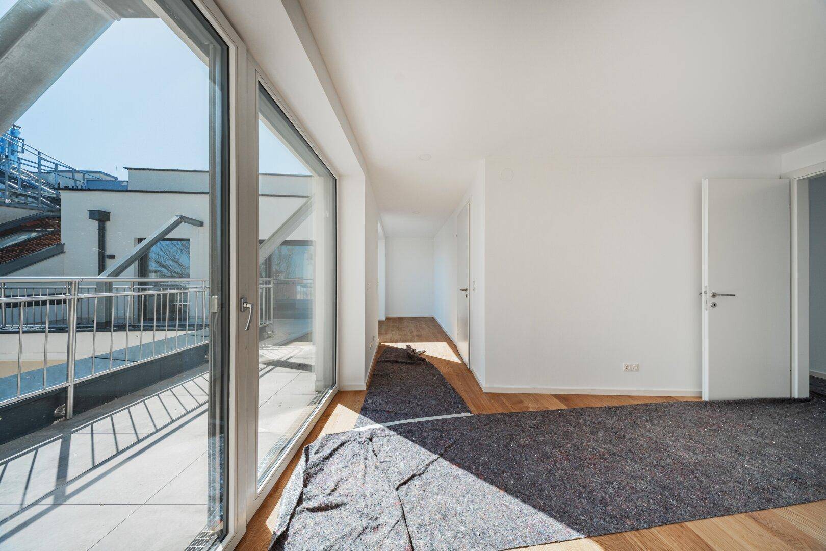 Langer, heller Flur mit Holzboden und großen Fensterfronten, die den Raum mit Licht füllen.
